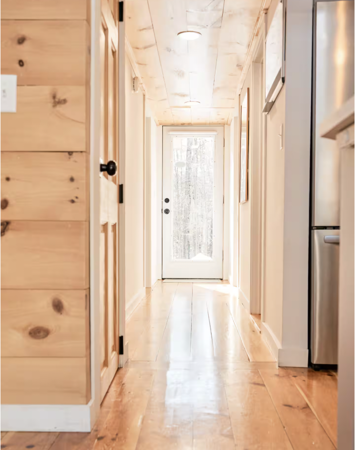 Bright hallway in a cozy home with wooden walls, hardwood flooring, and a glass door at the end leading outside.