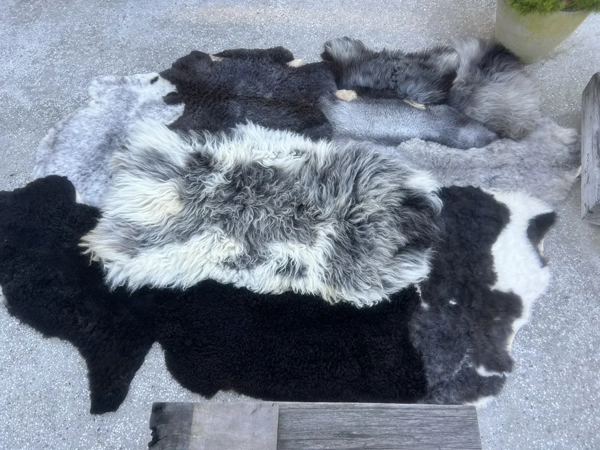 Dotje is a black and grey patchwork sheepskin rug (102 x 67 in.) with black, charcoal and silver pelts around a shaggy white-and-grey center.