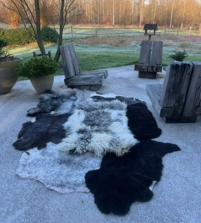 Dotje is a black and grey patchwork sheepskin rug (102 x 67 in.) with black, charcoal and silver pelts around a shaggy white-and-grey center.