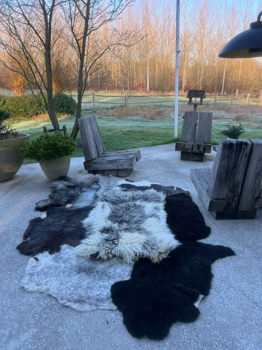 Dotje is a black and grey patchwork sheepskin rug (102 x 67 in.) with black, charcoal and silver pelts around a shaggy white-and-grey center.