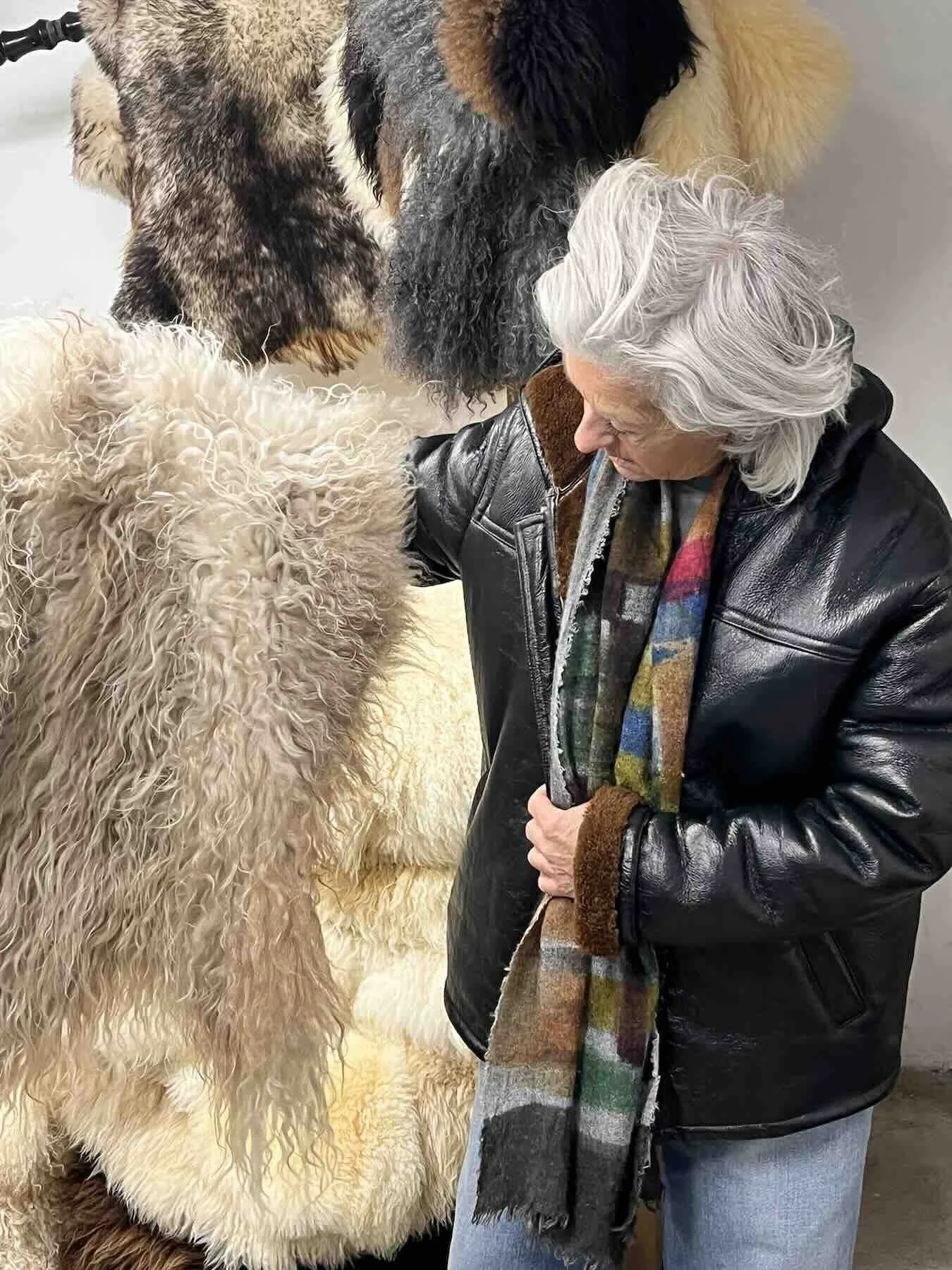 Artist Sabine Maes examines hanging cream, grey, and dark brown pelts for a Wol Society sheep skin rug