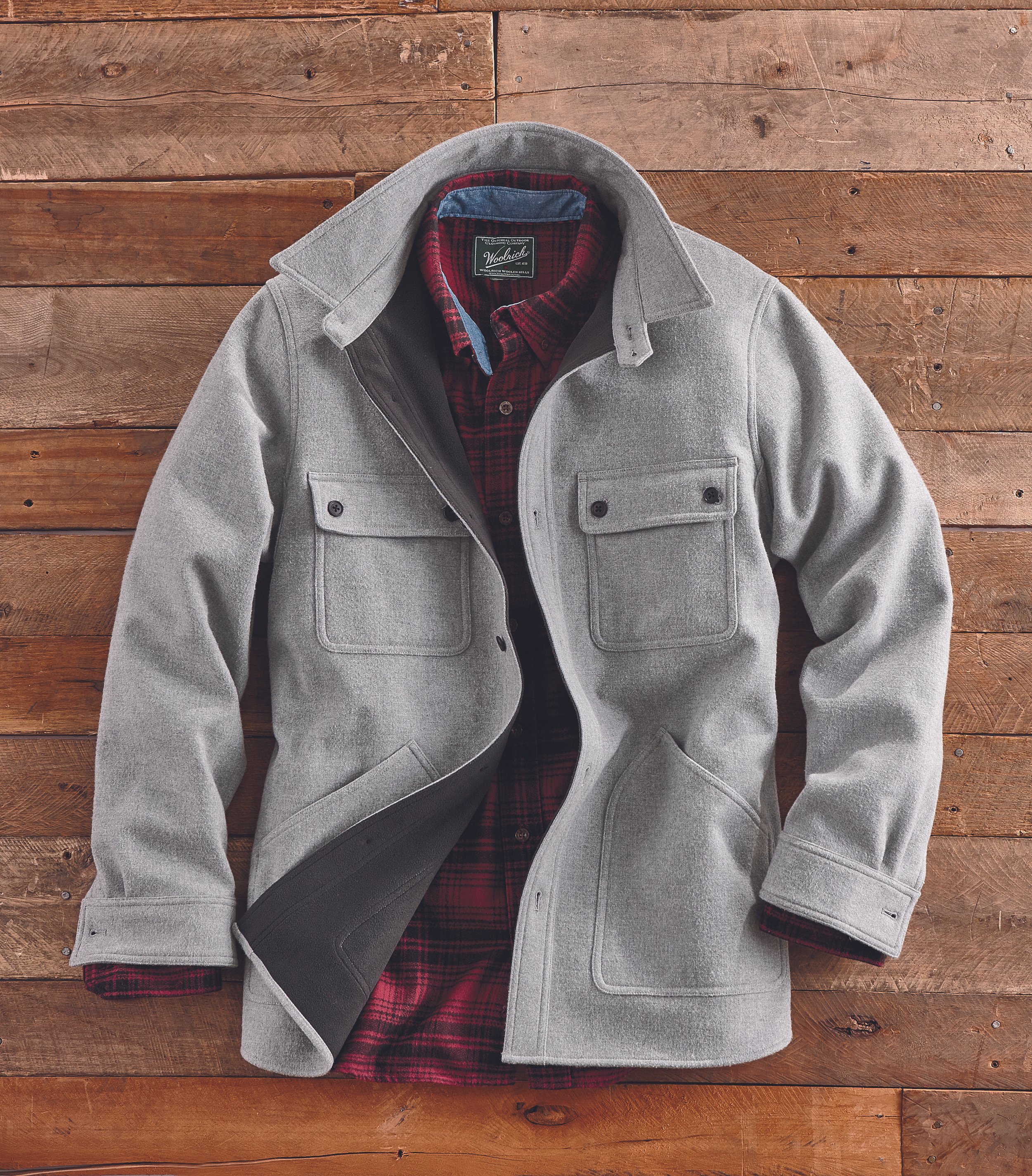A gray wool coat with a red and black plaid shirt underneath, laid out on a wooden surface.