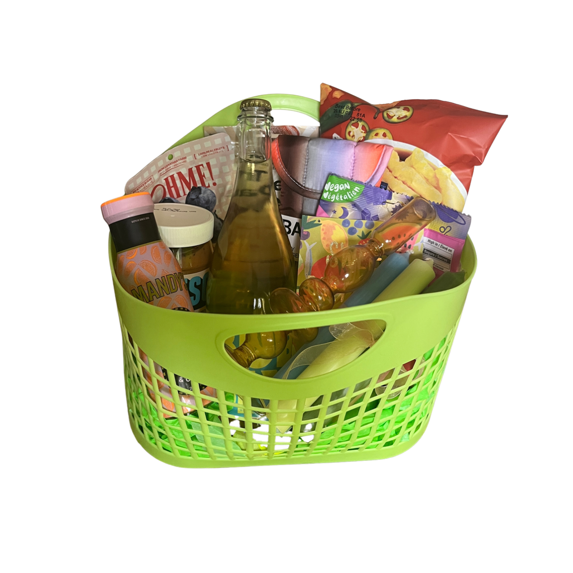 A green plastic basket filled with snacks, beverages, and party items, including chips, a glass bottle, and decorated items.