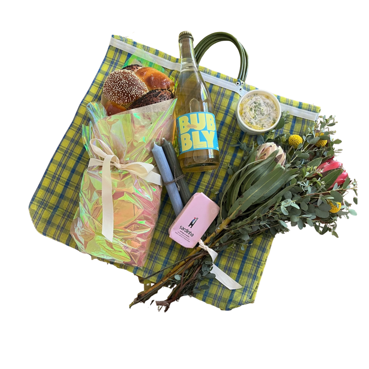 A picnic setup with a checkered green and yellow mat, containing a bouquet of flowers, a wrapped gift with a white ribbon, a bottle labeled 'BUBBLY,' a container of dip, a pink lighter, and some cupcakes, along with a bouquet of eucalyptus and pink flowers.