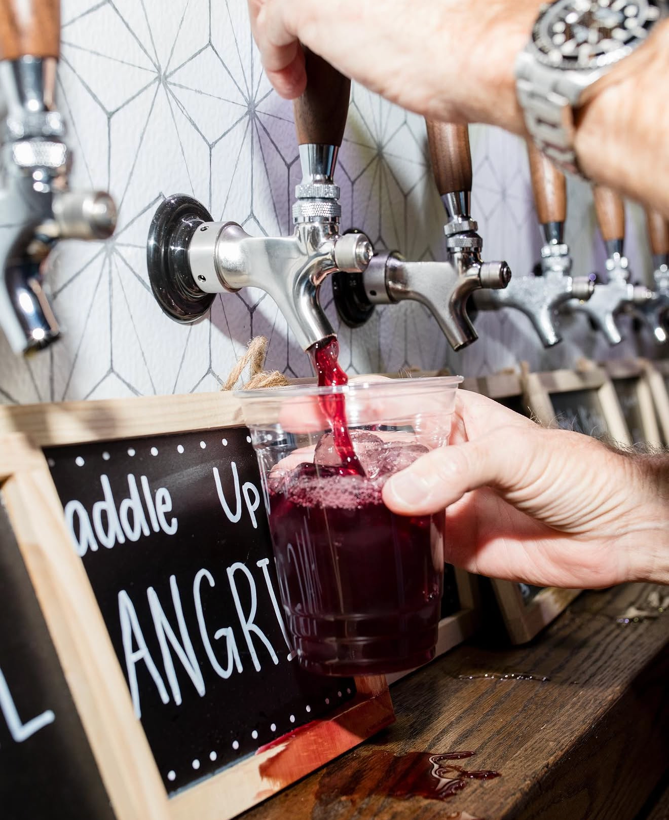 Person pouring red wine from a tap into a clear plastic cup at a wine bar.