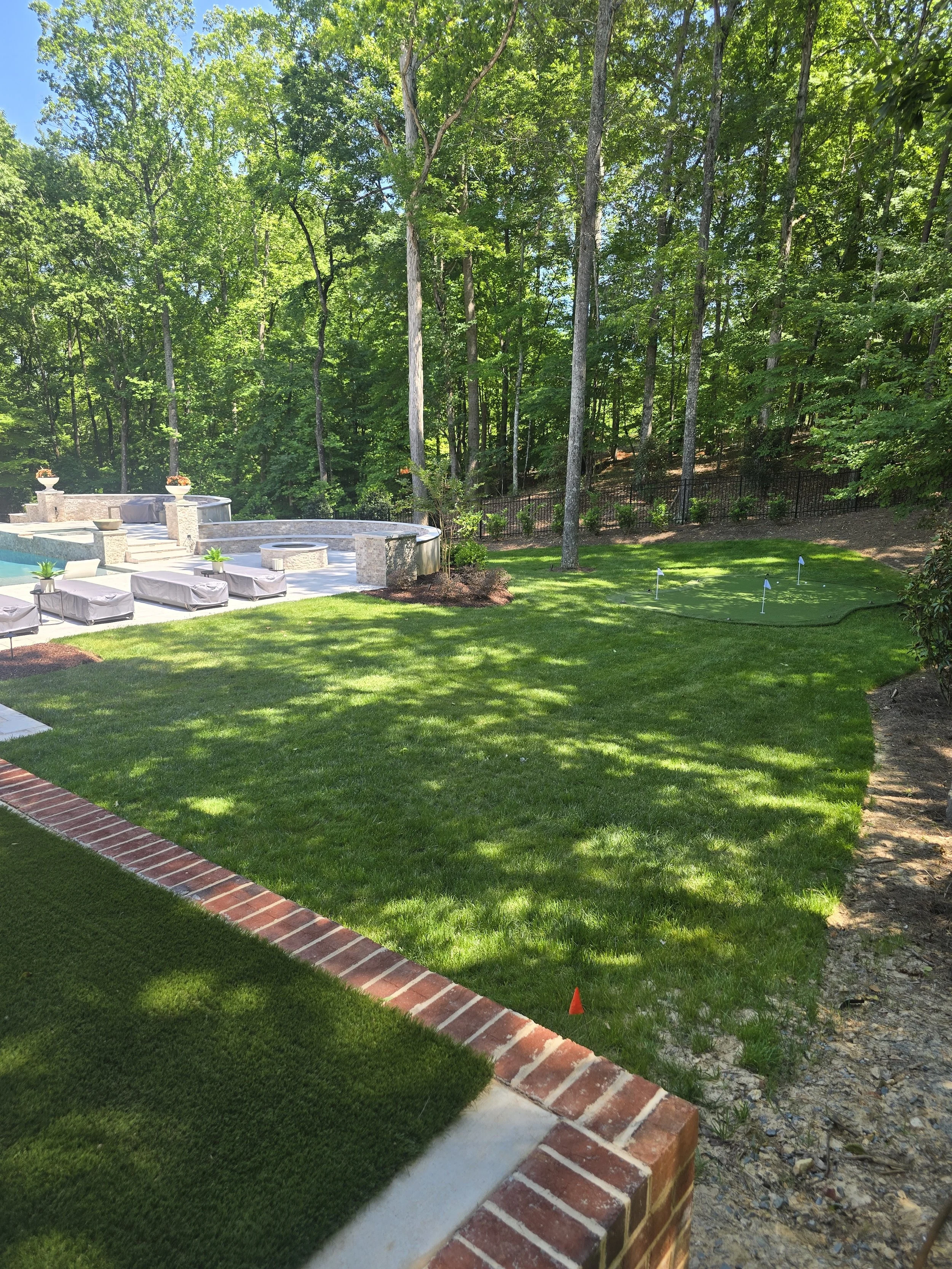 Landscaped backyard by The Kiker Group near Monroe, NC, featuring a spacious lawn, brick border, patio seating, and mature trees.