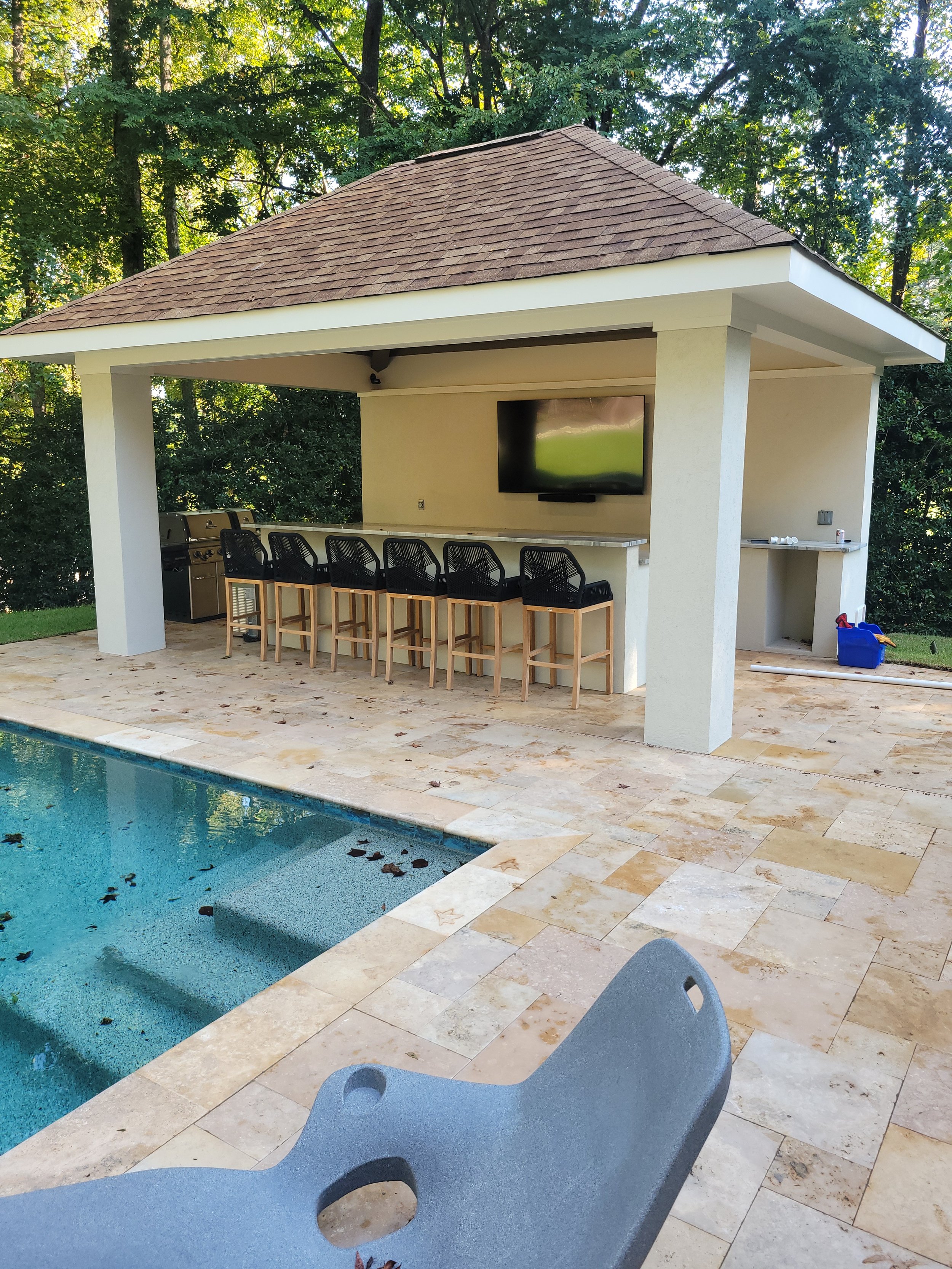 Custom backyard by The Kiker Group near Monroe, NC, featuring a swimming pool and covered outdoor gazebo with a grill, television, and bar seating.