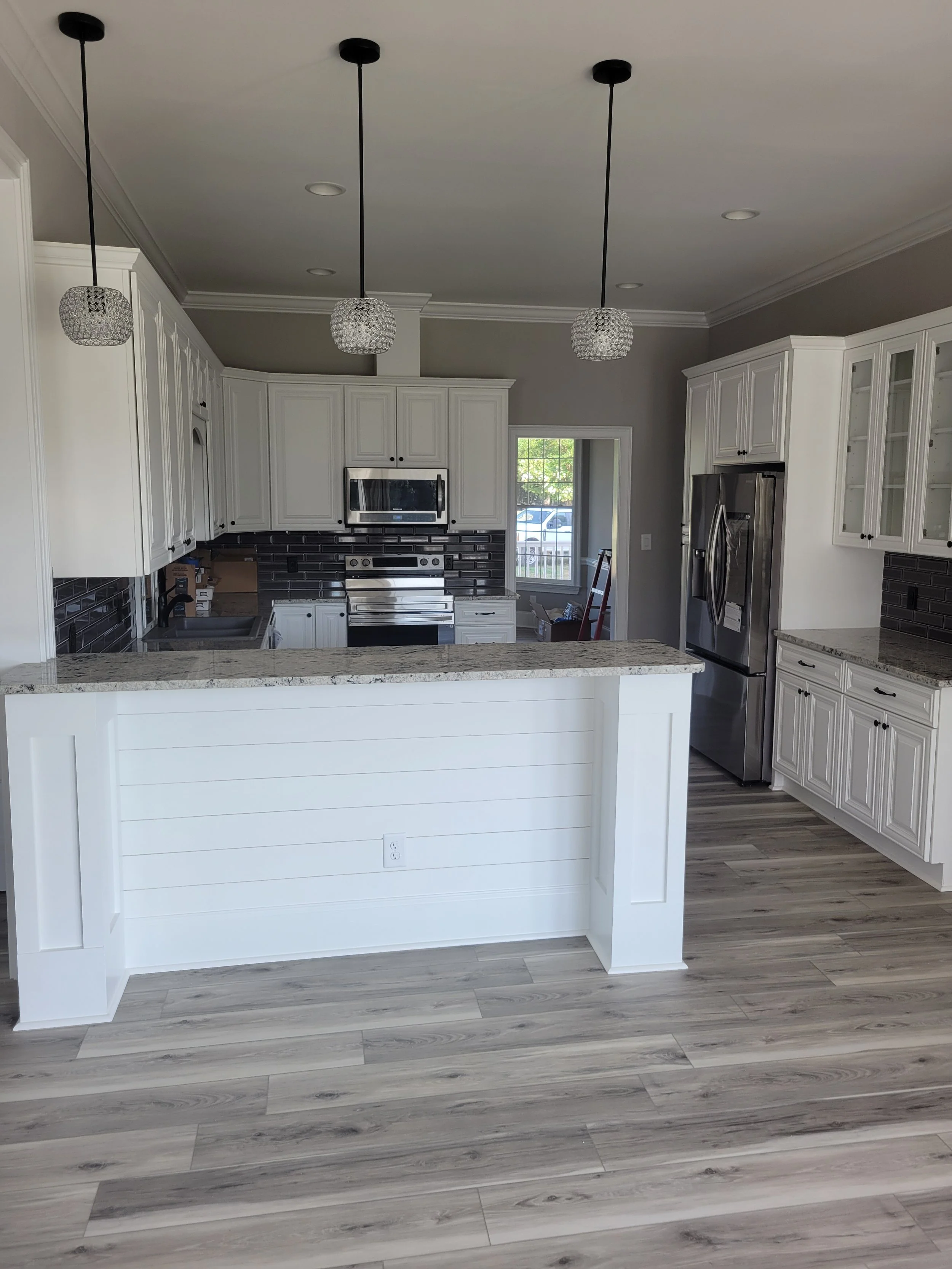 Modern custom home kitchen by The Kiker Group in Monroe, NC, with white cabinetry, black backsplash, stainless steel appliances, and a large island with pendant lighting.
