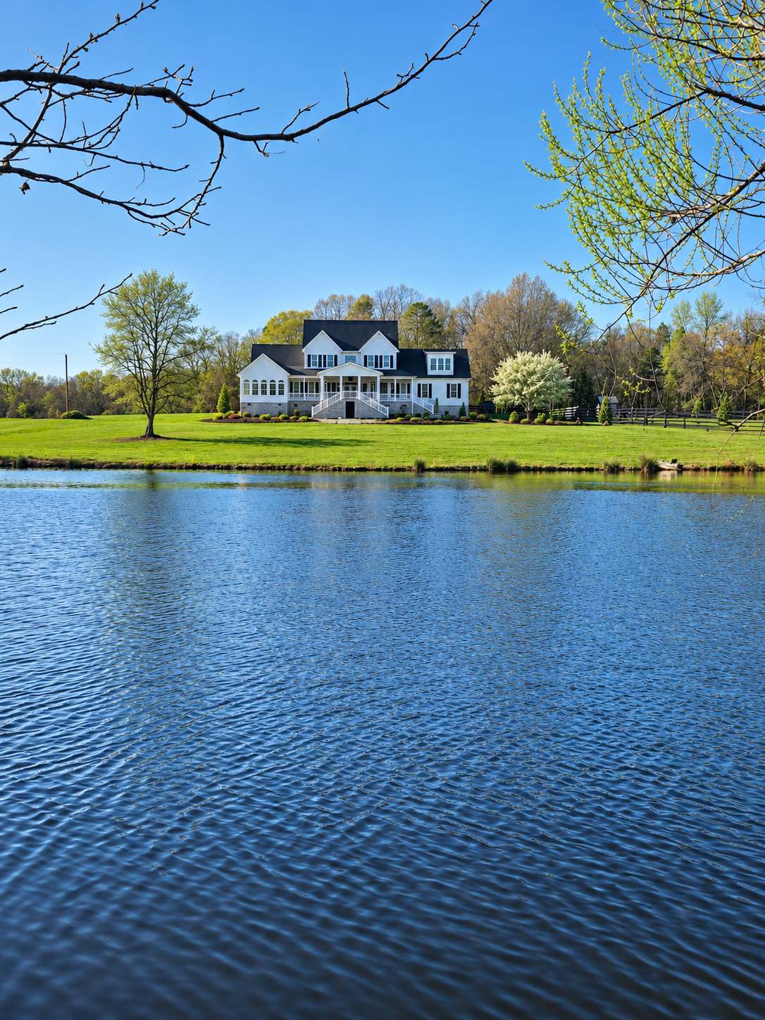 White custom waterfront home by The Kiker Group near Monroe, NC, surrounded by mature trees and a landscaped green lawn.