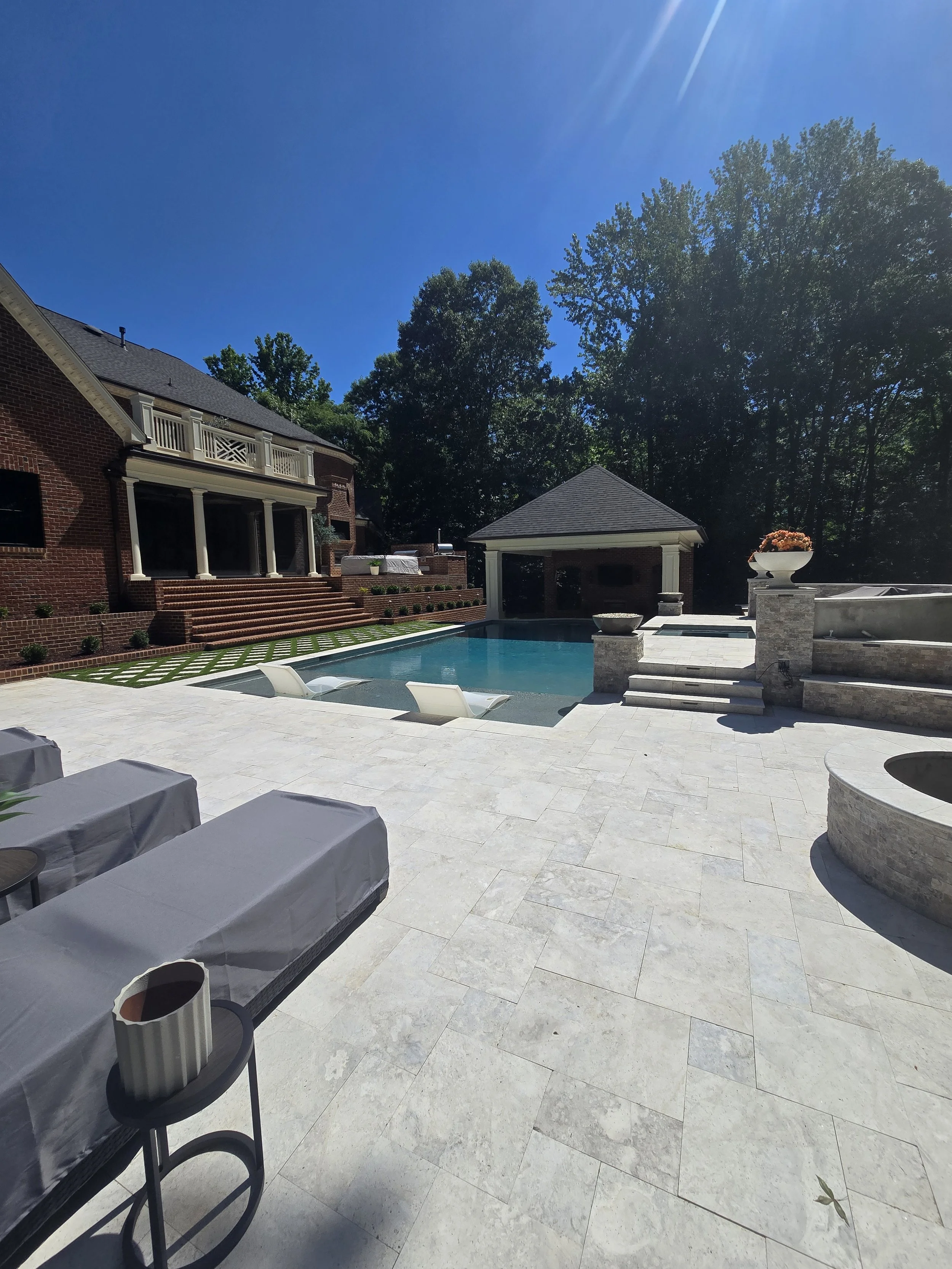 Custom backyard by The Kiker Group near Monroe, NC, featuring a swimming pool, brick home, covered pavilion, balcony, and outdoor entertaining areas.