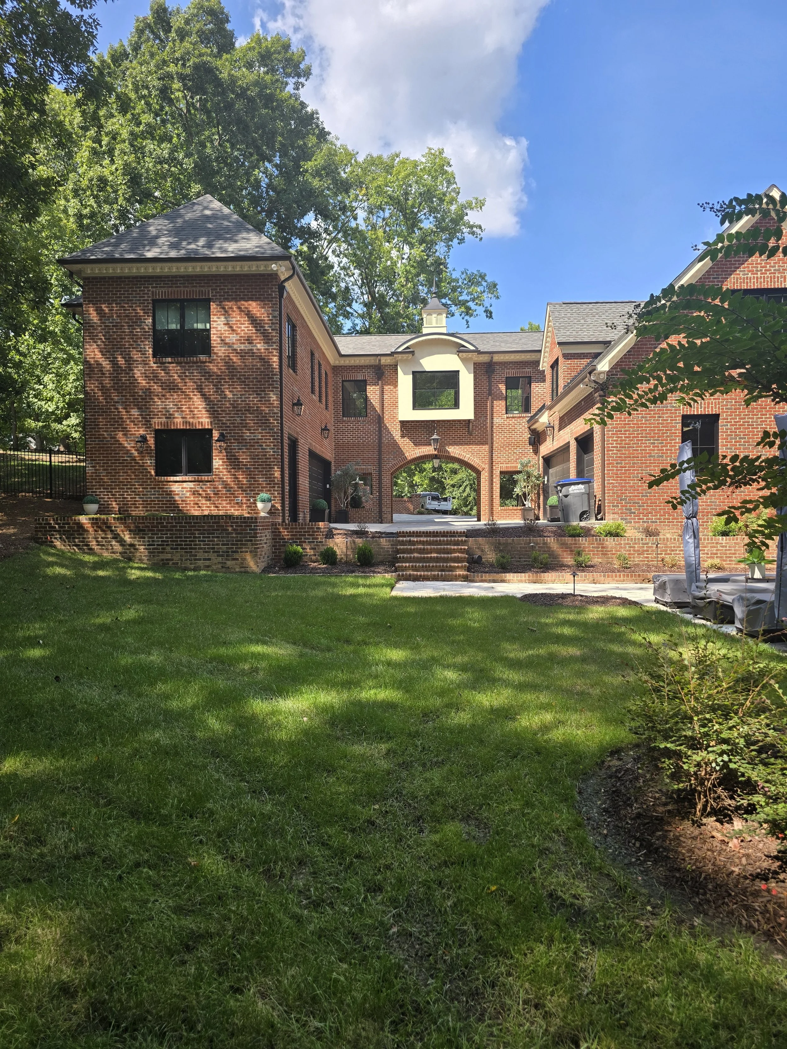 Red brick custom home by The Kiker Group near Monroe, NC, featuring a central archway, spacious driveway, mature trees, and landscaped lawn.