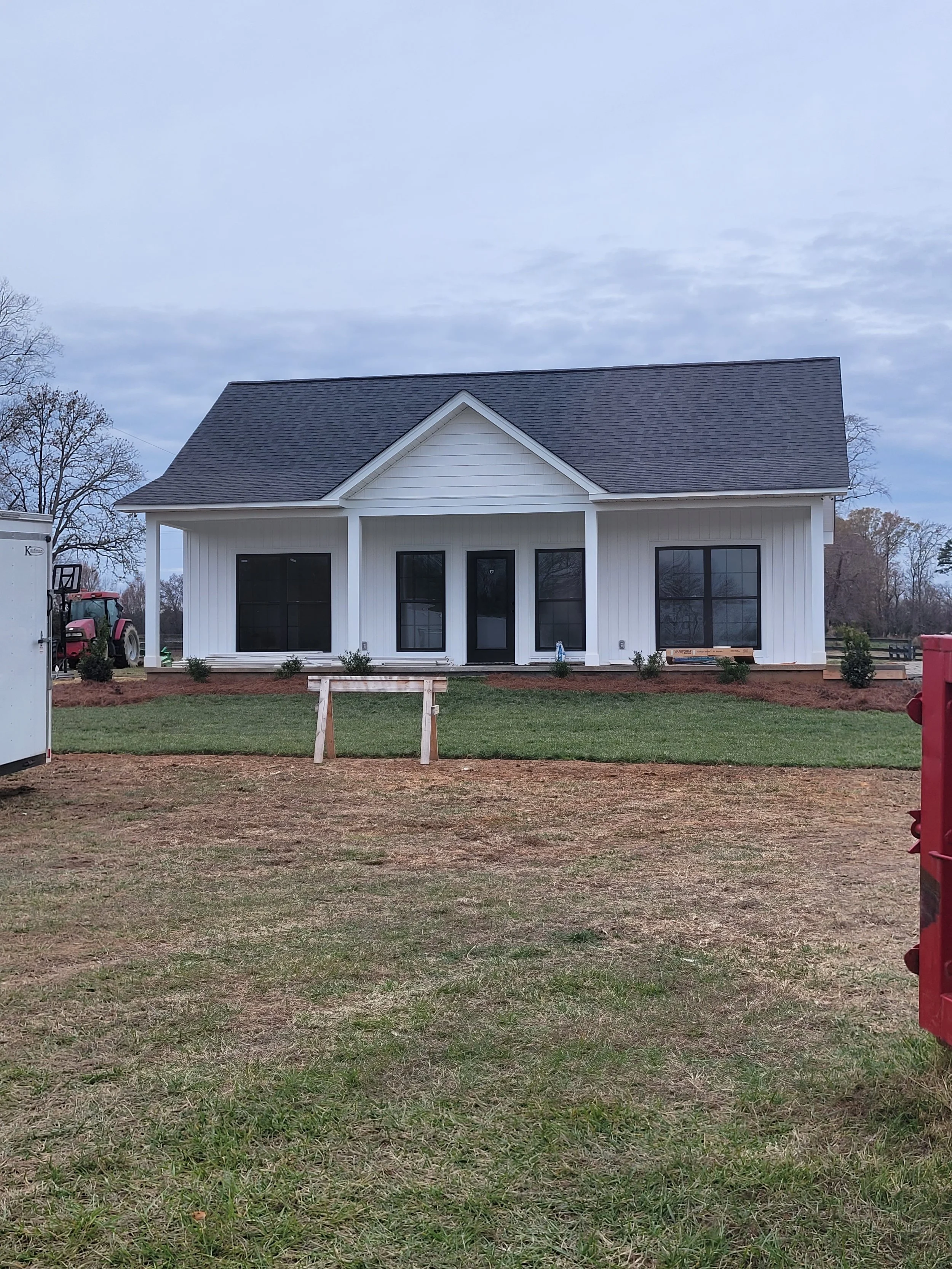 Newly built white custom home by The Kiker Group near Monroe, NC, featuring black windows, a dark gray roof, and a spacious rural setting.