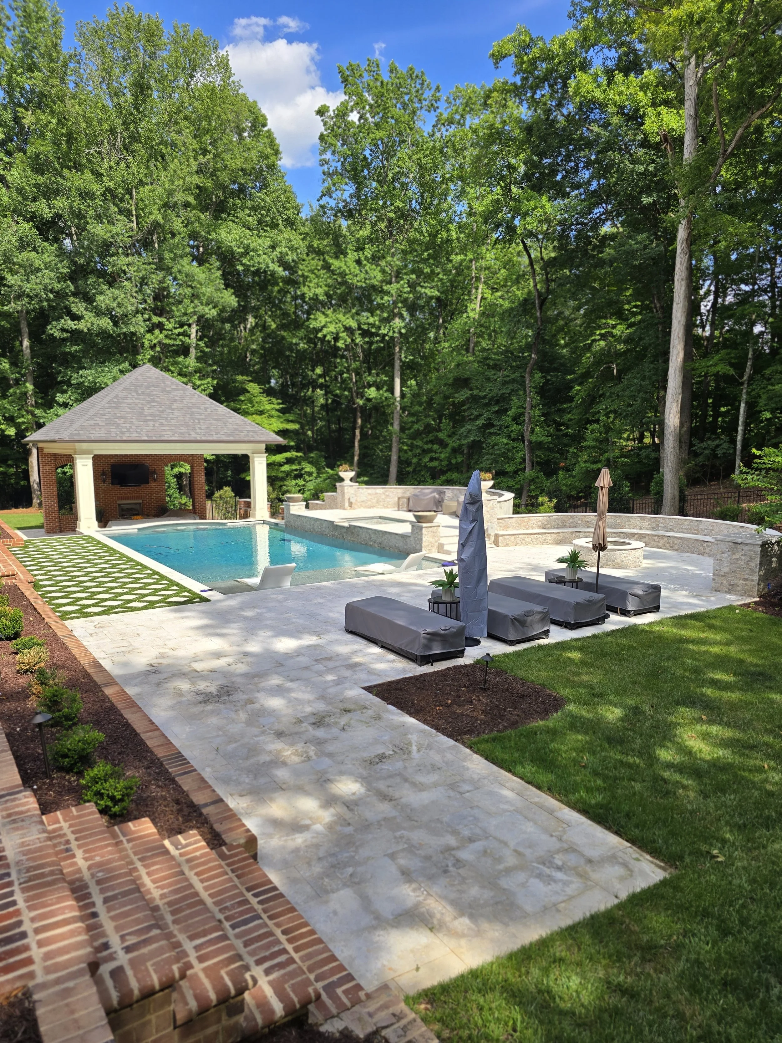 Custom outdoor living space by The Kiker Group near Monroe, NC, featuring a swimming pool, patio seating, firepit, and covered porch.