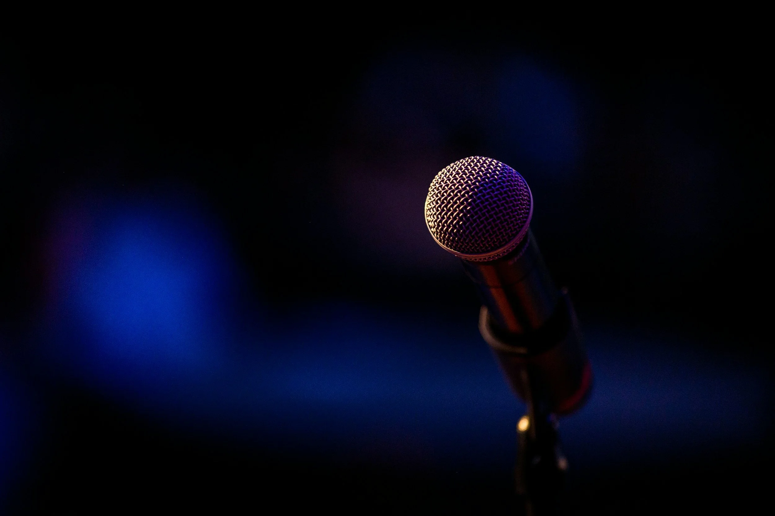 A close-up of a microphone illuminated by purple and blue lights against a dark background.