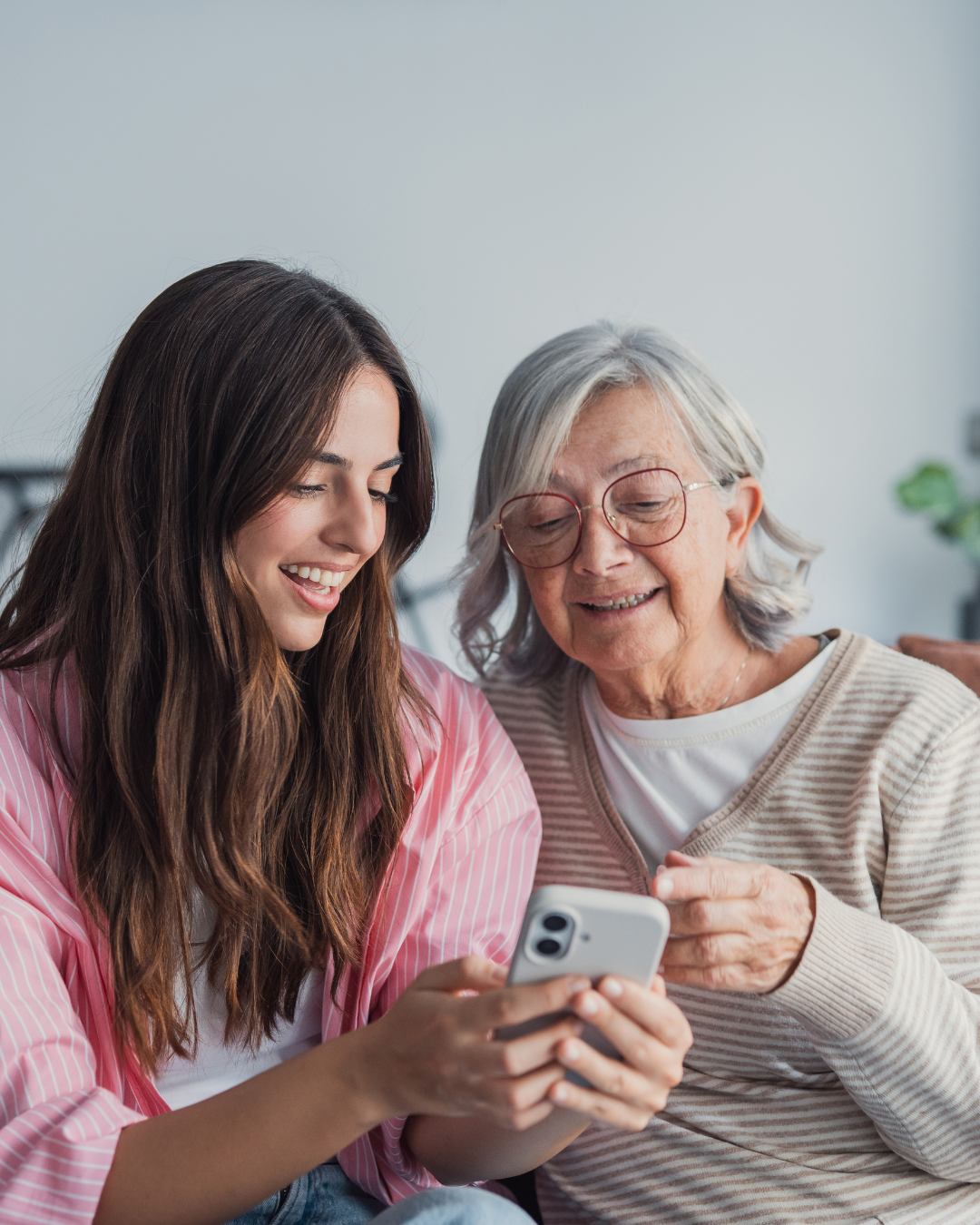 A young woman and an elderly woman are looking at a smartphone together, smiling and sharing a moment of joy.