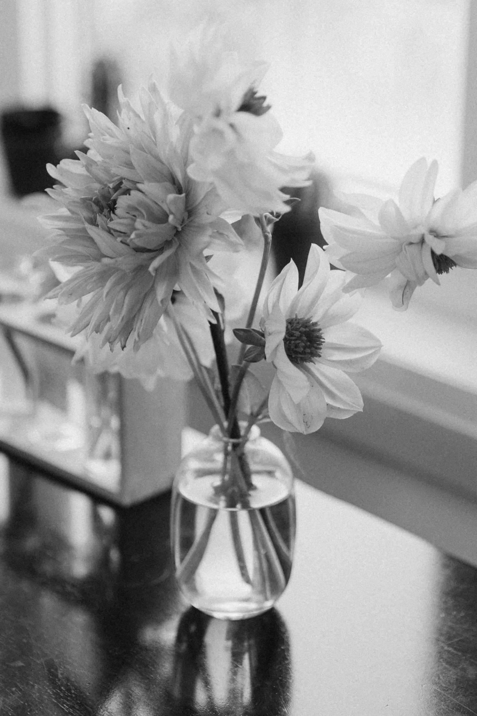 Black and white photo of a small bouquet of flowers in a glass vase on a table.