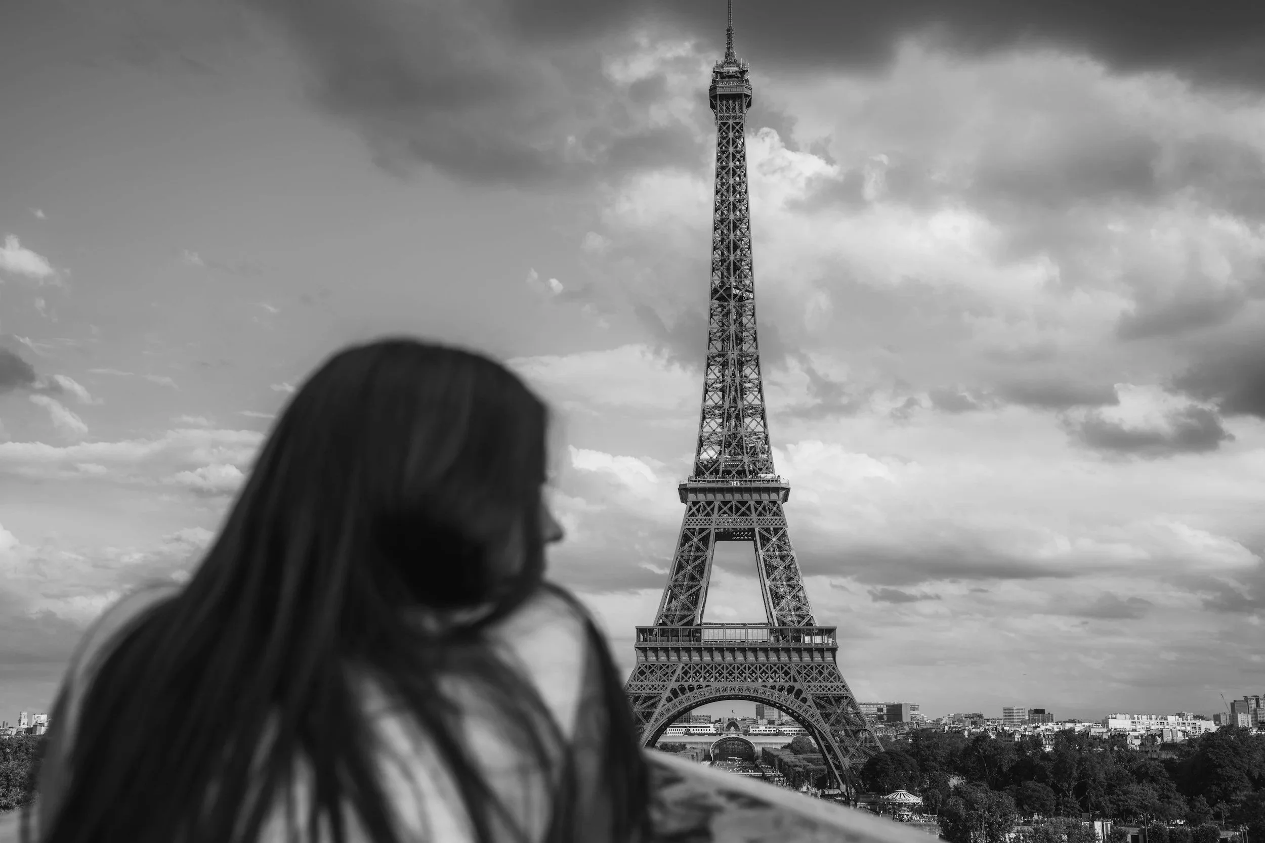 A woman with long hair looking at the Eiffel Tower in Paris during cloudy weather.