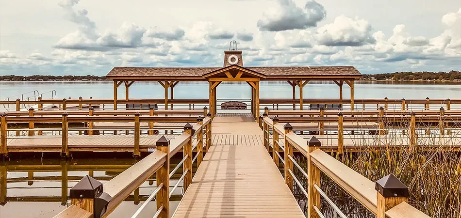 Wooden pier leading to a covered pavilion over a body of water, with railings on both sides and a cloudy sky above.