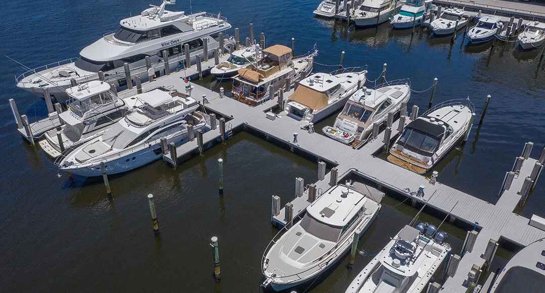 Aerial view of a marina with several luxury boats and yachts docked at wooden piers in calm water.