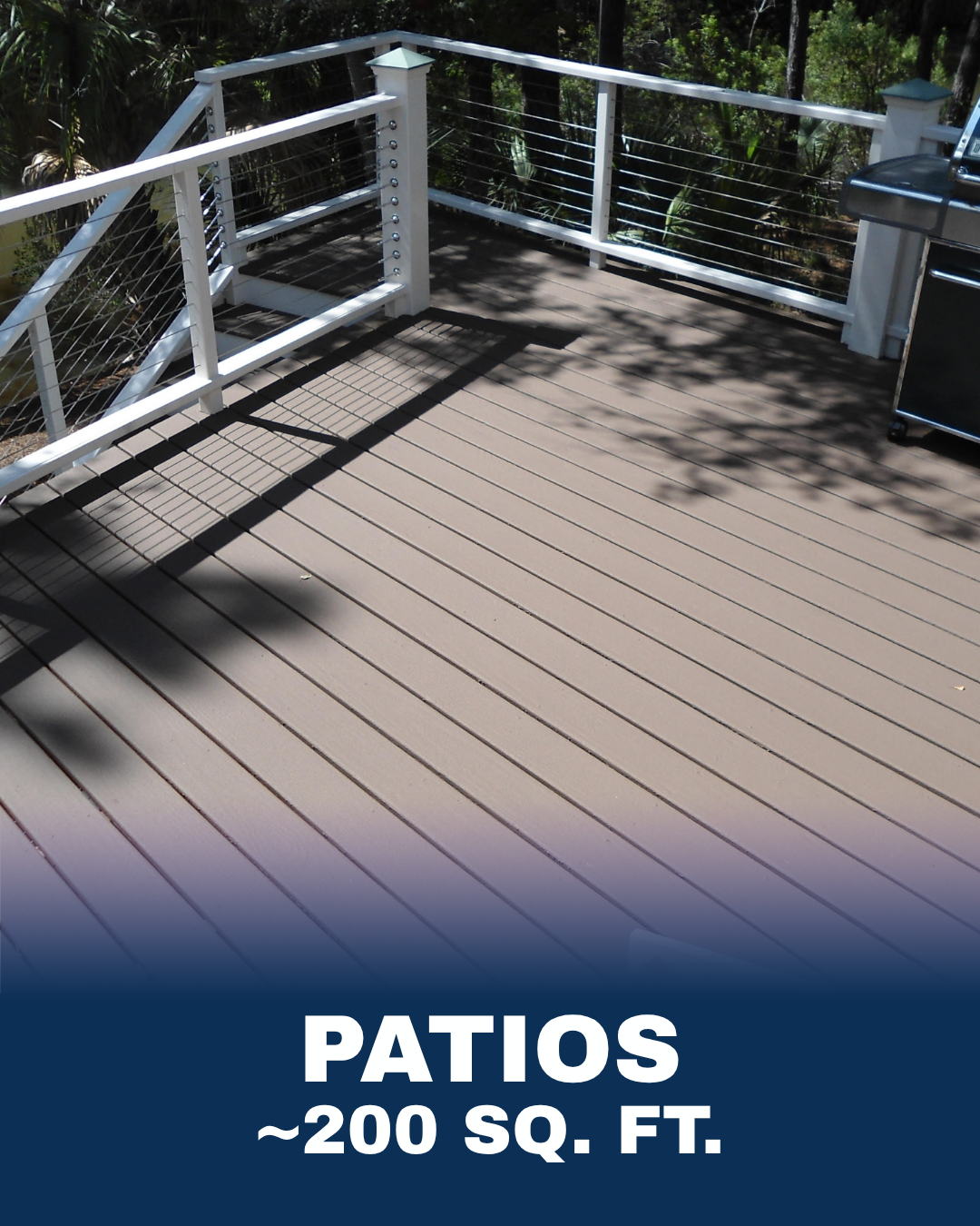 A spacious outdoor patio with wood decking, white railing with metal wires, surrounded by trees and greenery. A grill is visible on the right side.