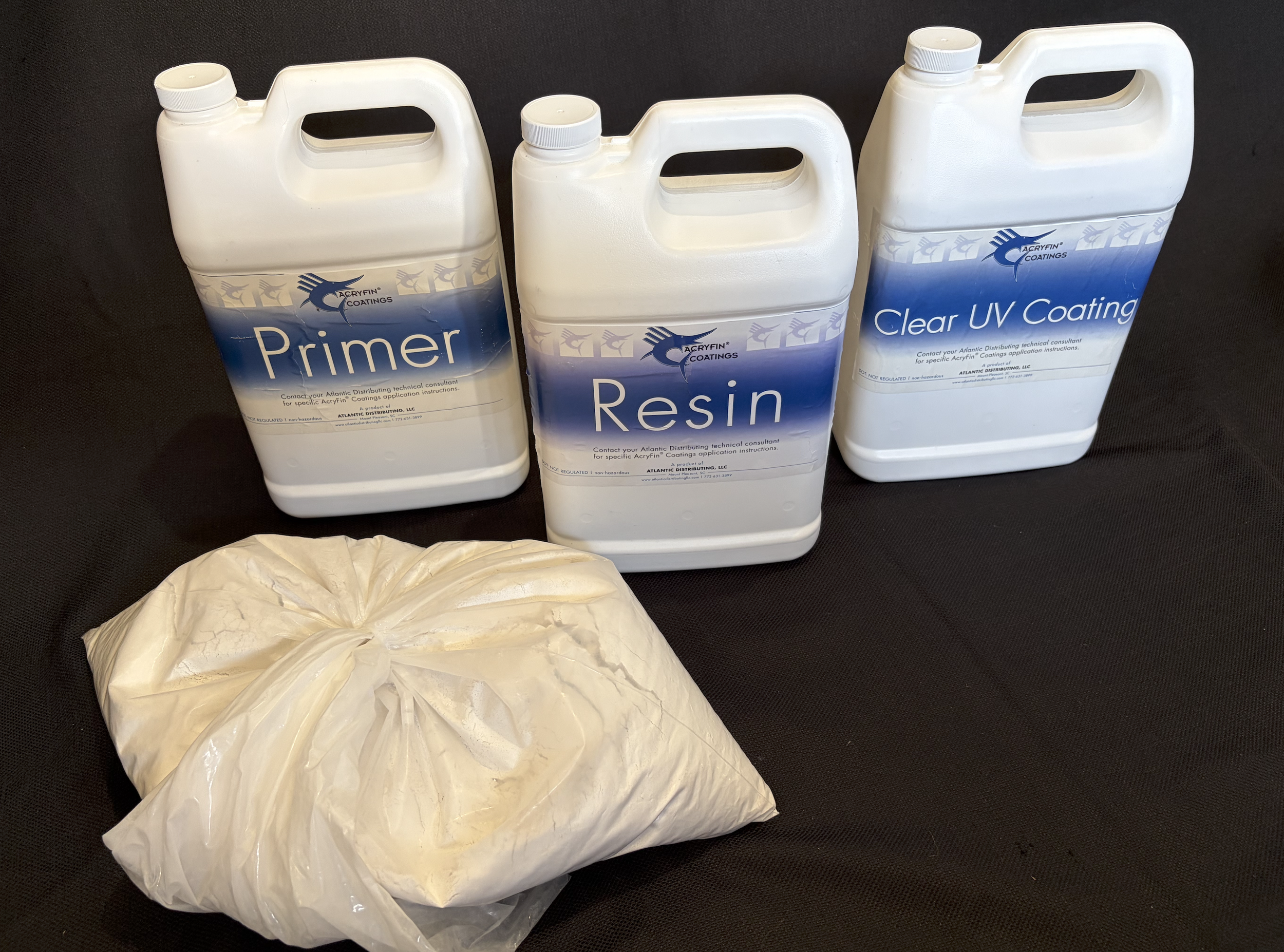 Three white plastic containers labeled Primer, Resin, and Clear UV Coating from Acryfin Coatings, and a large plastic bag filled with a light-colored substance, all placed on a black surface.