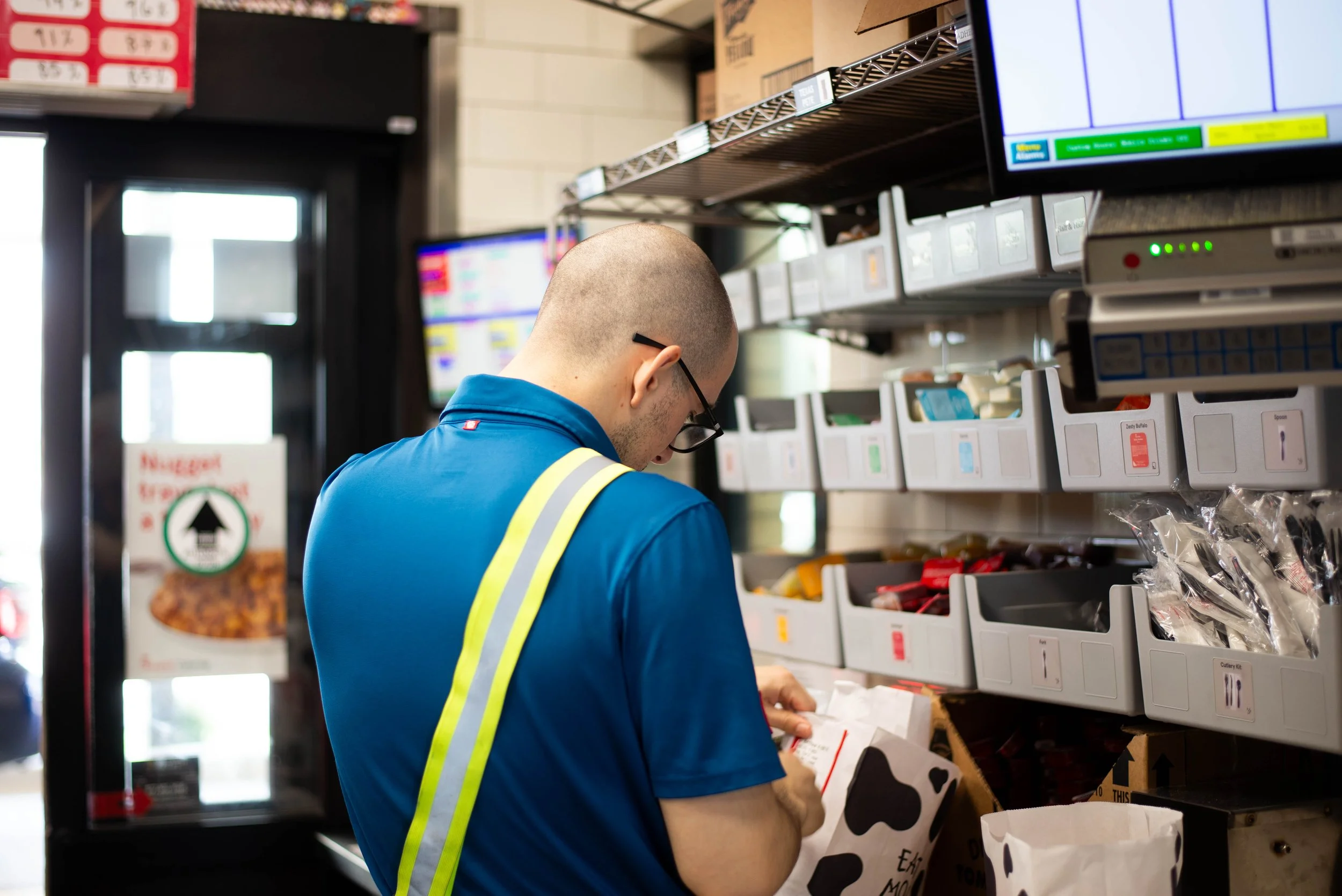 A person wearing a blue shirt with reflective yellow stripes is shopping in a grocery store, looking at items on the shelves.
