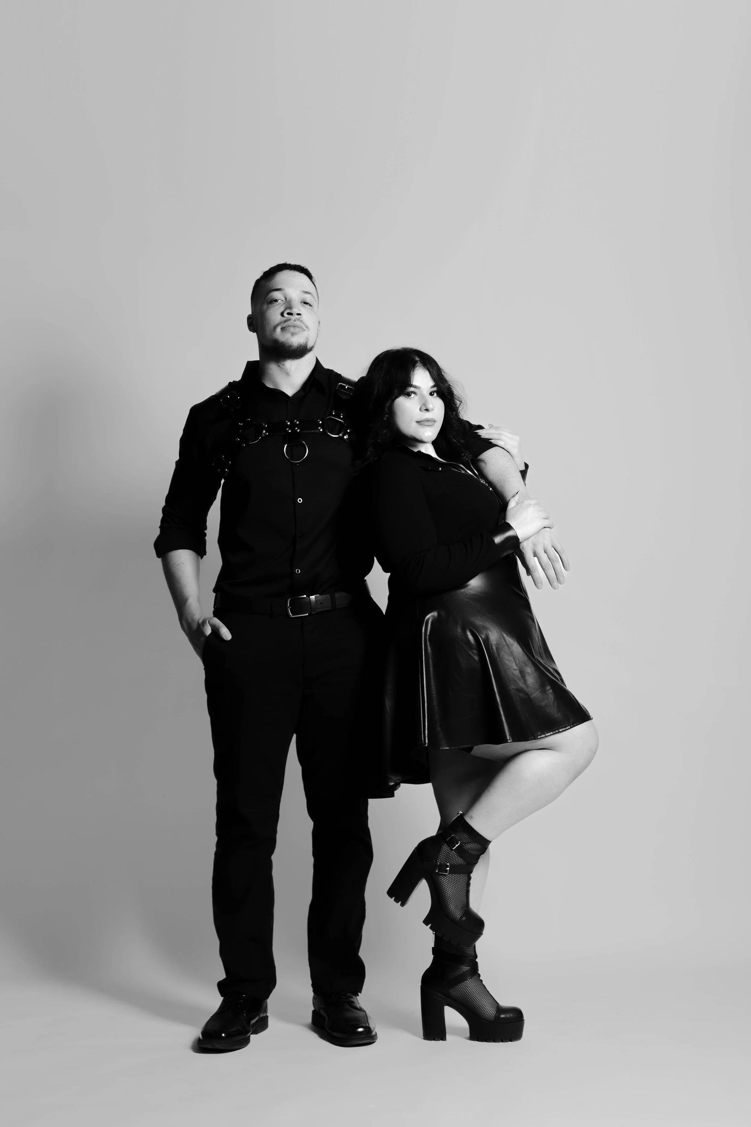 Black and white studio portrait of a couple standing together in dark outfits