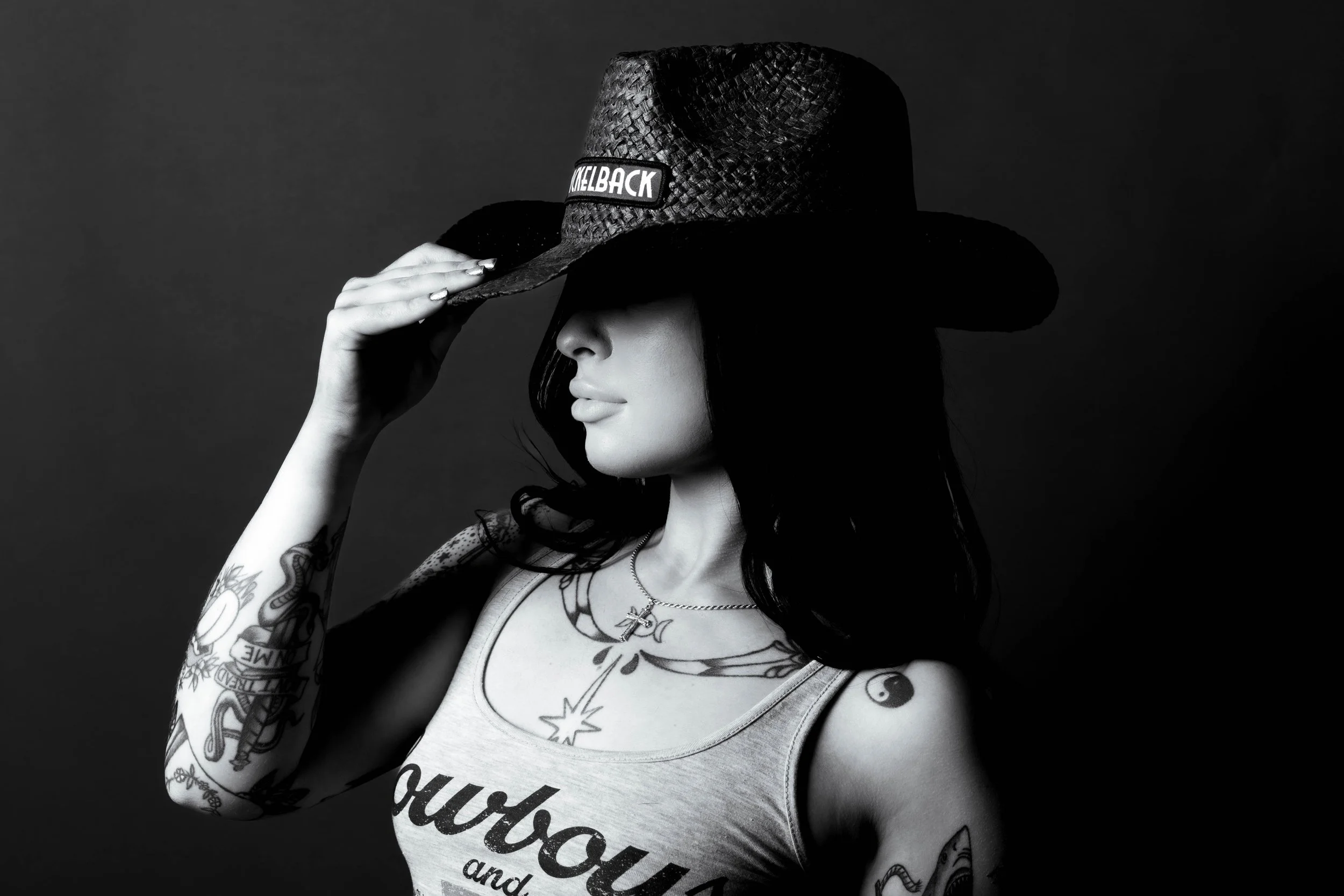 Black and white portrait of a woman in a straw cowboy hat pulling the brim over her eyes