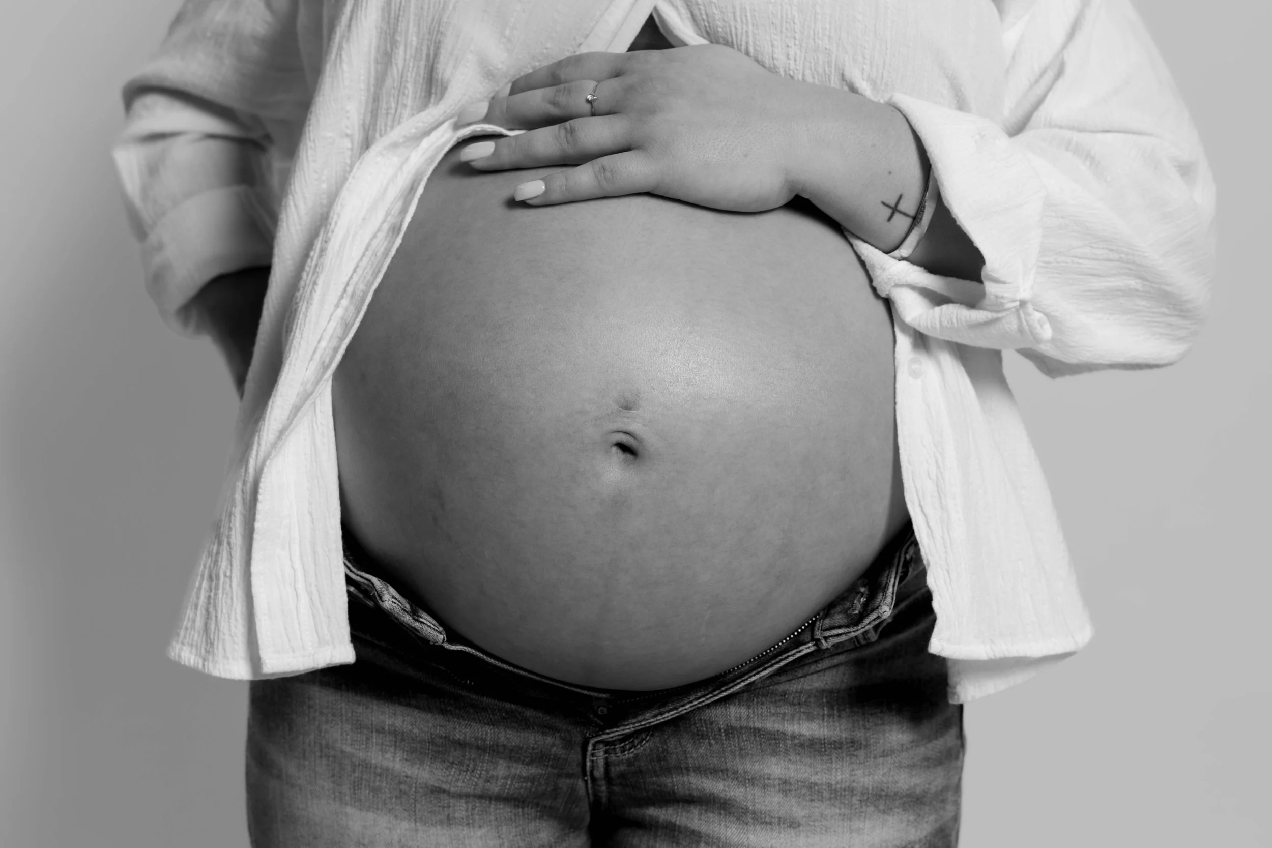 Black and white close up of hands cradling a bare baby bump, maternity photography by Lillie Ruth