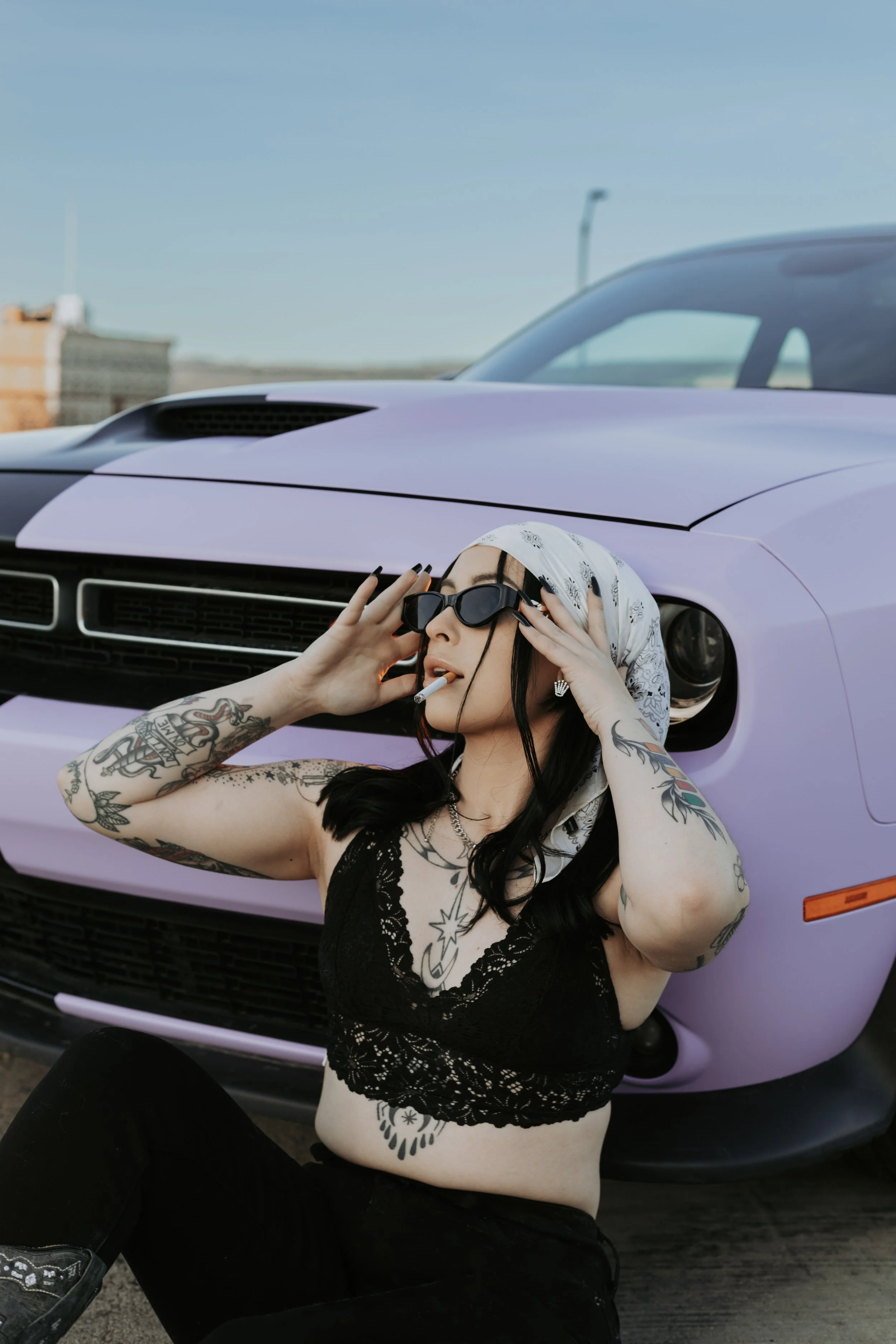 Tattooed woman in sunglasses posing in front of a purple Dodge Challenger