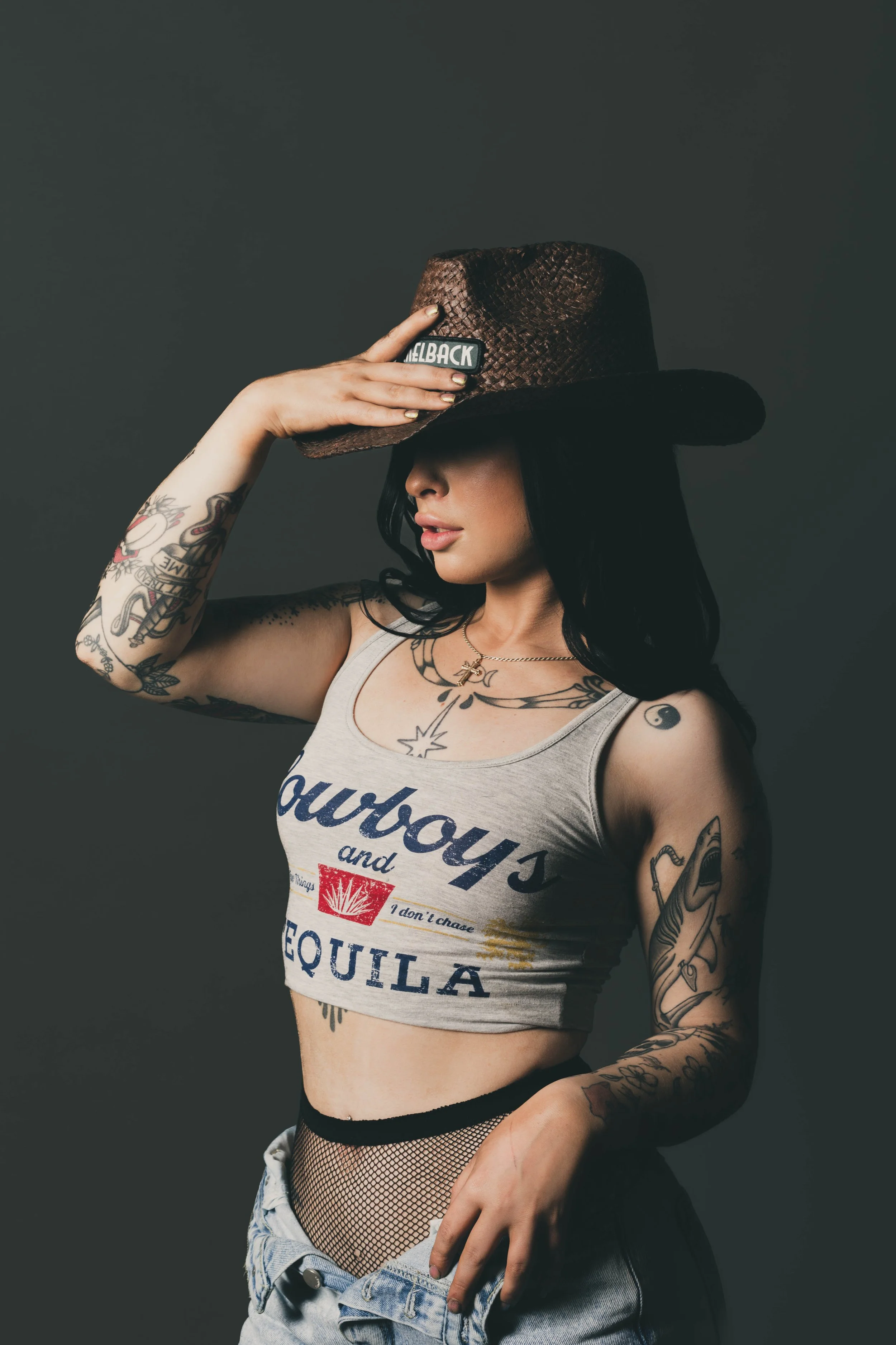 Tattooed woman in a cowboy hat and graphic tank top posing with her hand on the brim