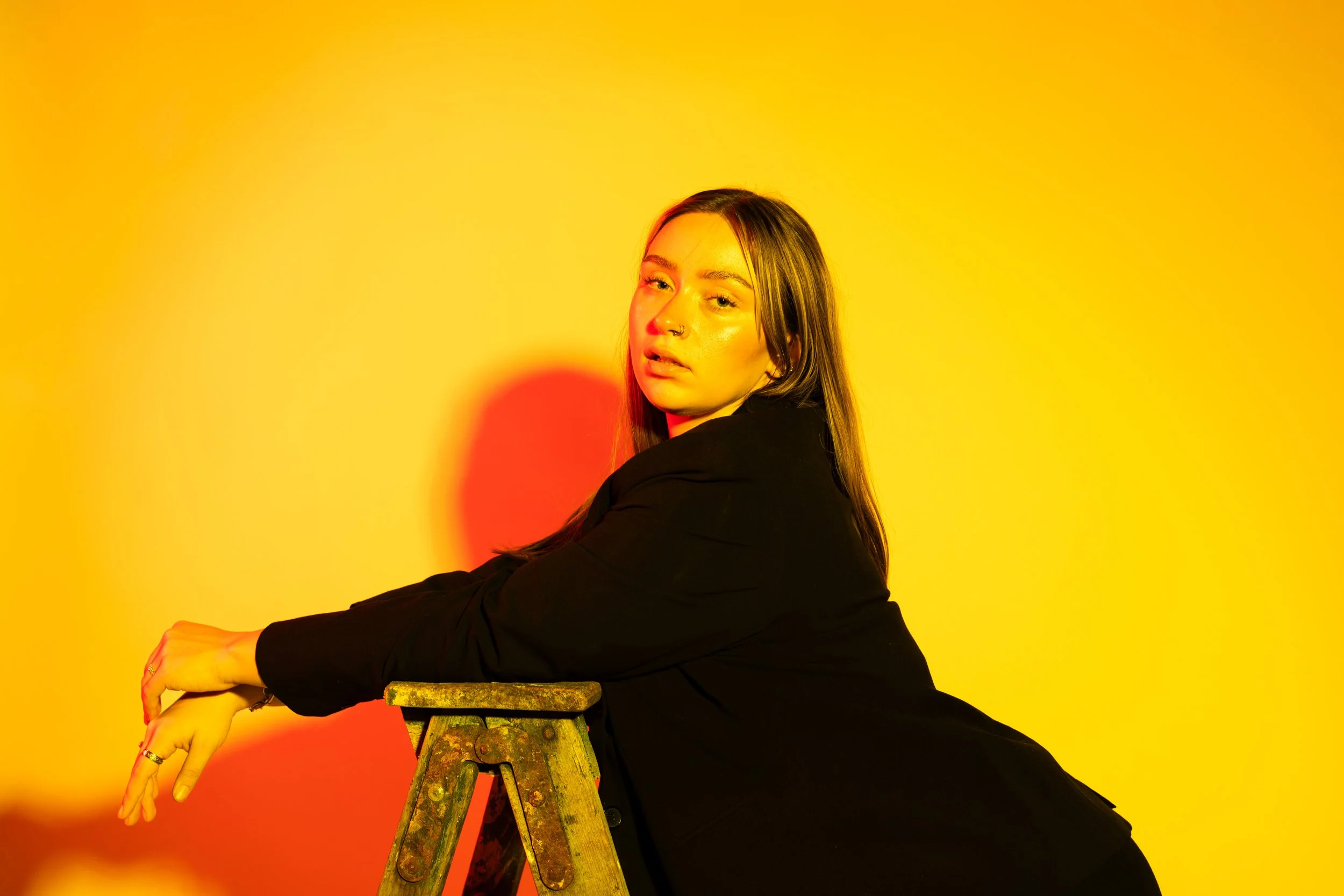 Woman glancing over her shoulder while seated on a stool under warm yellow studio lighting