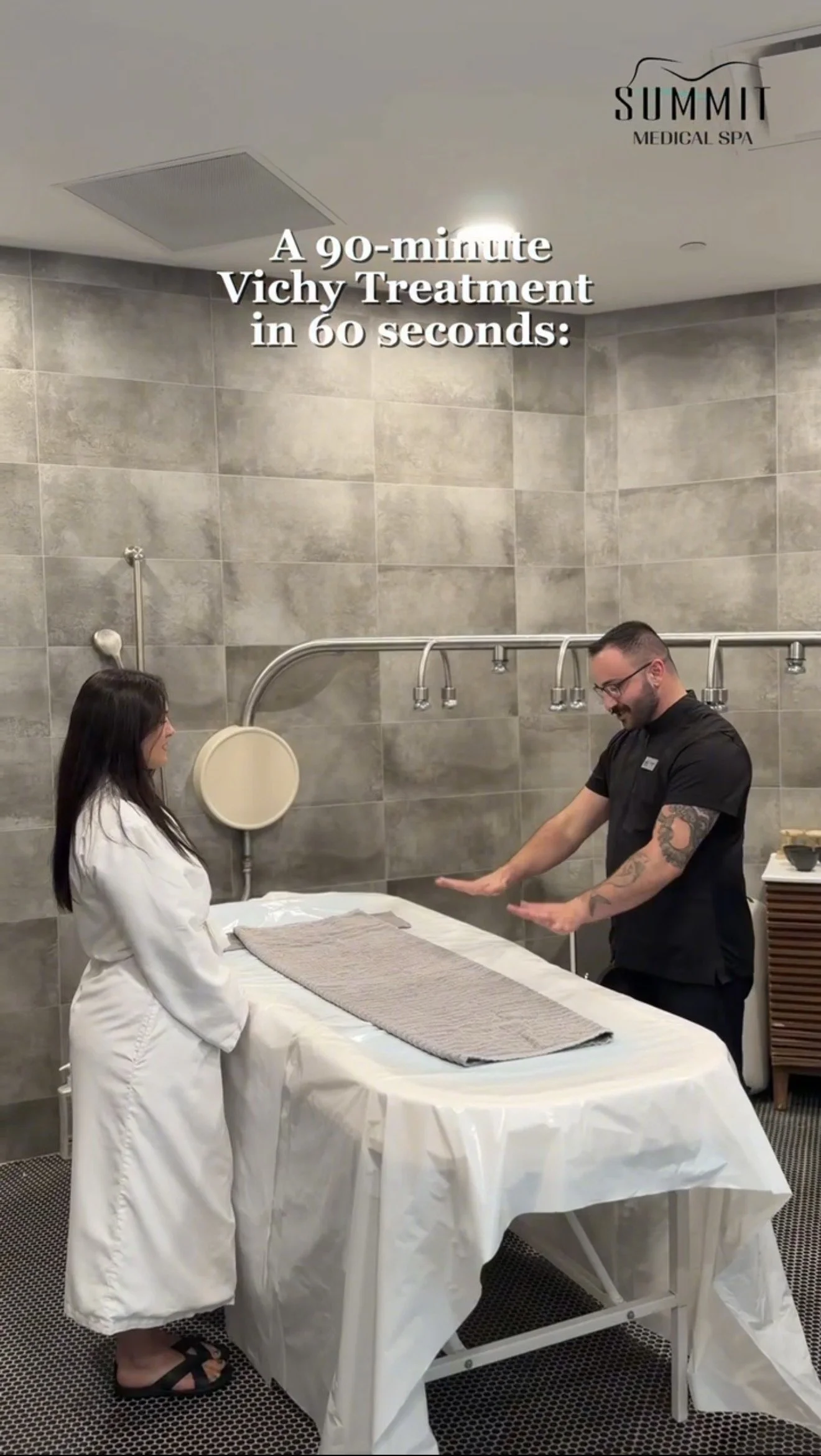 A woman in a white robe receiving a massage from a male therapist in a spa treatment room with tiled walls, a large massage table, and medical equipment, with text overlay promoting a 90-minute Vichy treatment.