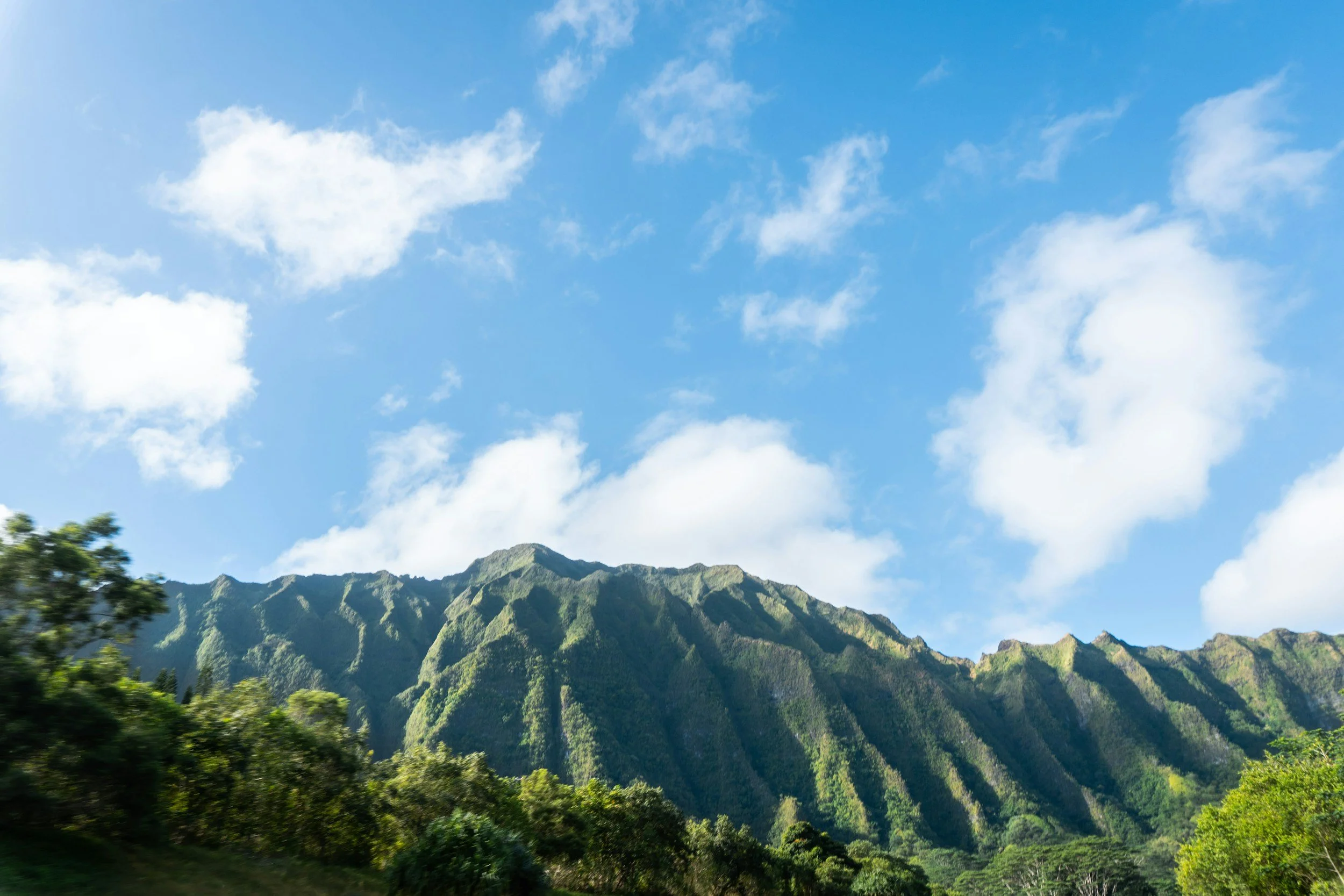 Green lush mountains with dense vegetation and a bright blue sky with scattered white clouds above.