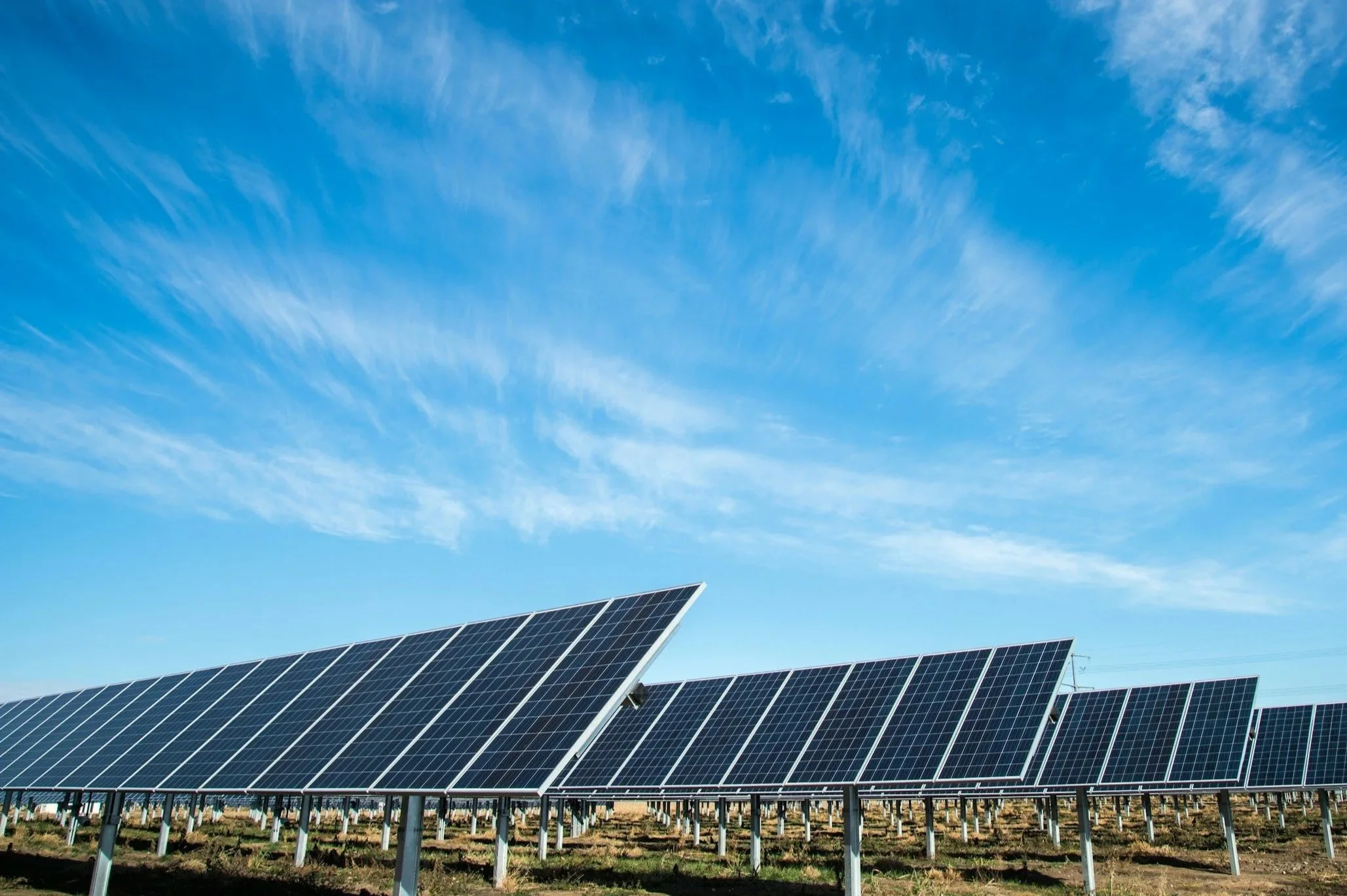 Solar panels installed in a field with a blue sky and wispy clouds overhead.