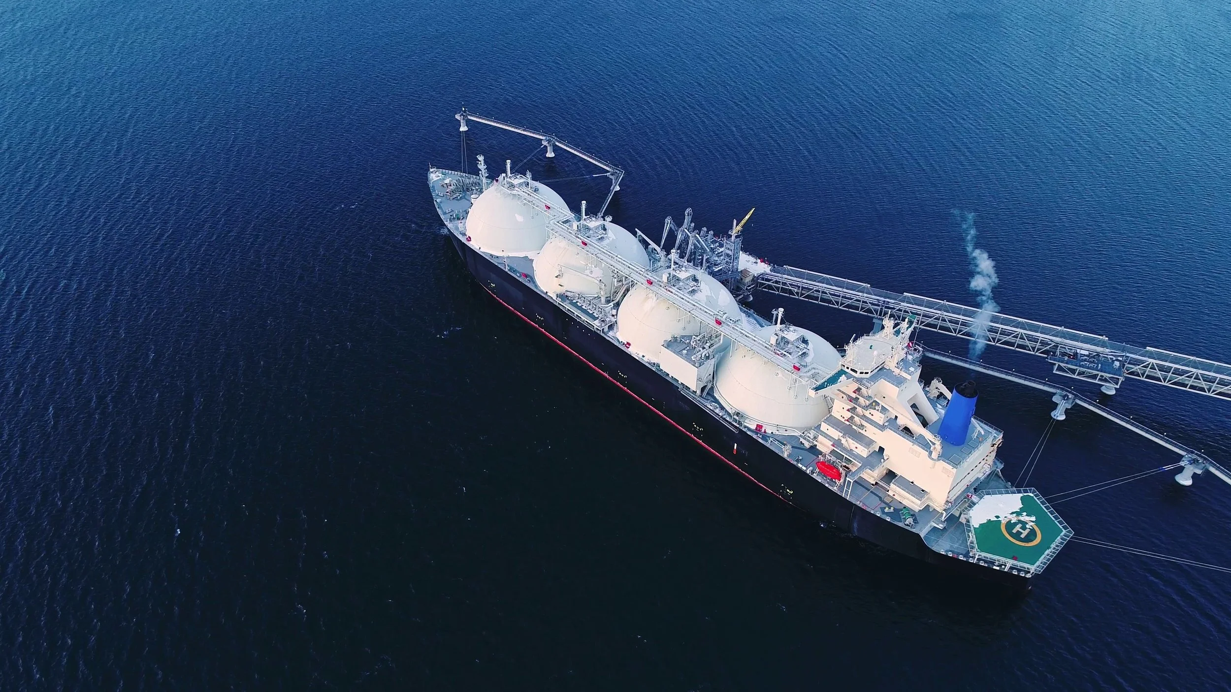 A large oil or gas drilling ship on the open ocean with a helipad at the stern.