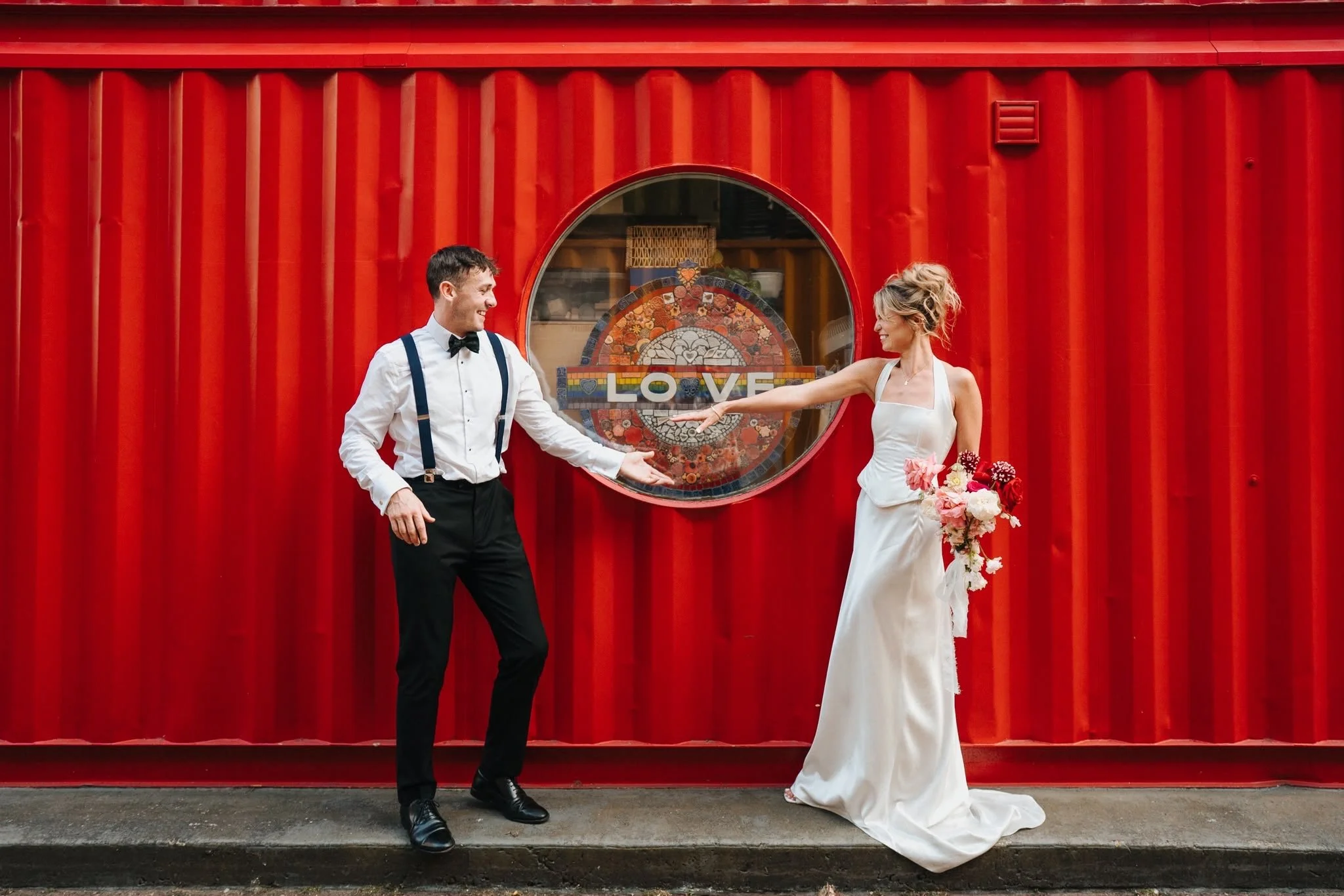 Earth Bridal bride and groom at a red shipping container, sustainable animal free wedding dress made in London