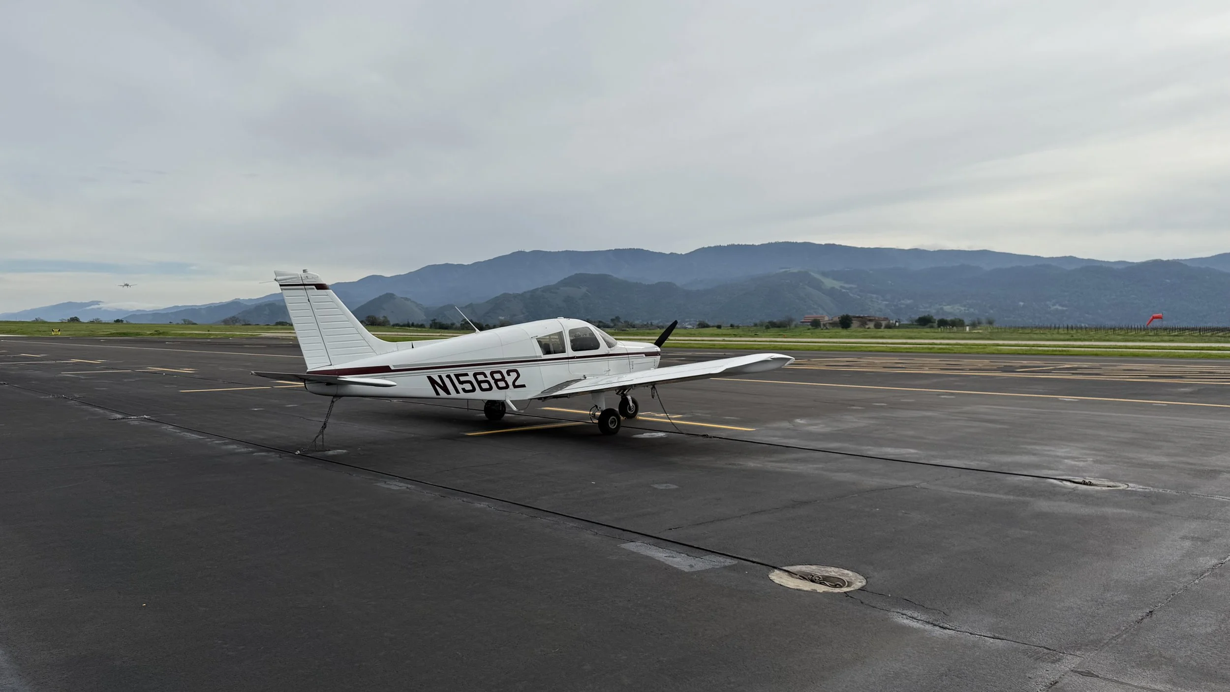Small white airplane with tail number N15682 parked on tarmac at an airport with mountains in the background under a cloudy sky.