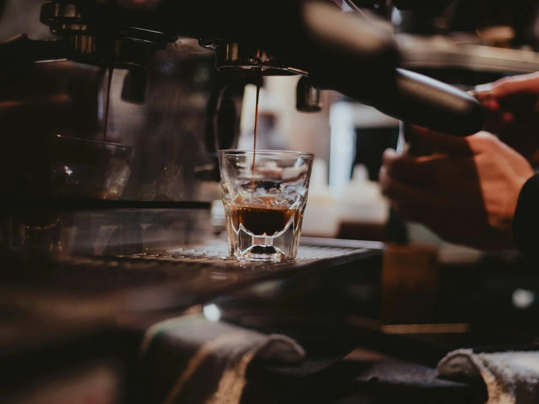 Coffee being brewed into a glass cup from an espresso machine.