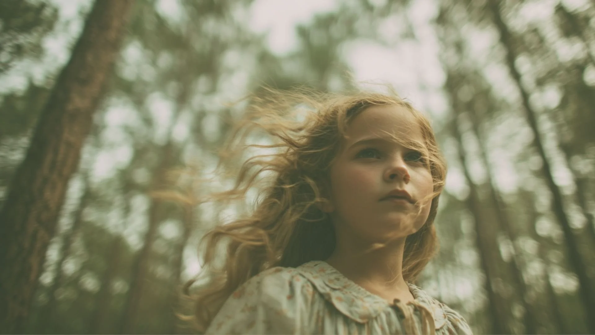 A young woman with long, wavy blonde hair gazing off into the distance in a forest with tall trees, soft natural light, and a slightly dreamy, ethereal atmosphere. Inspiration for the main character in the novel and screenplay Jojo and the Freaks