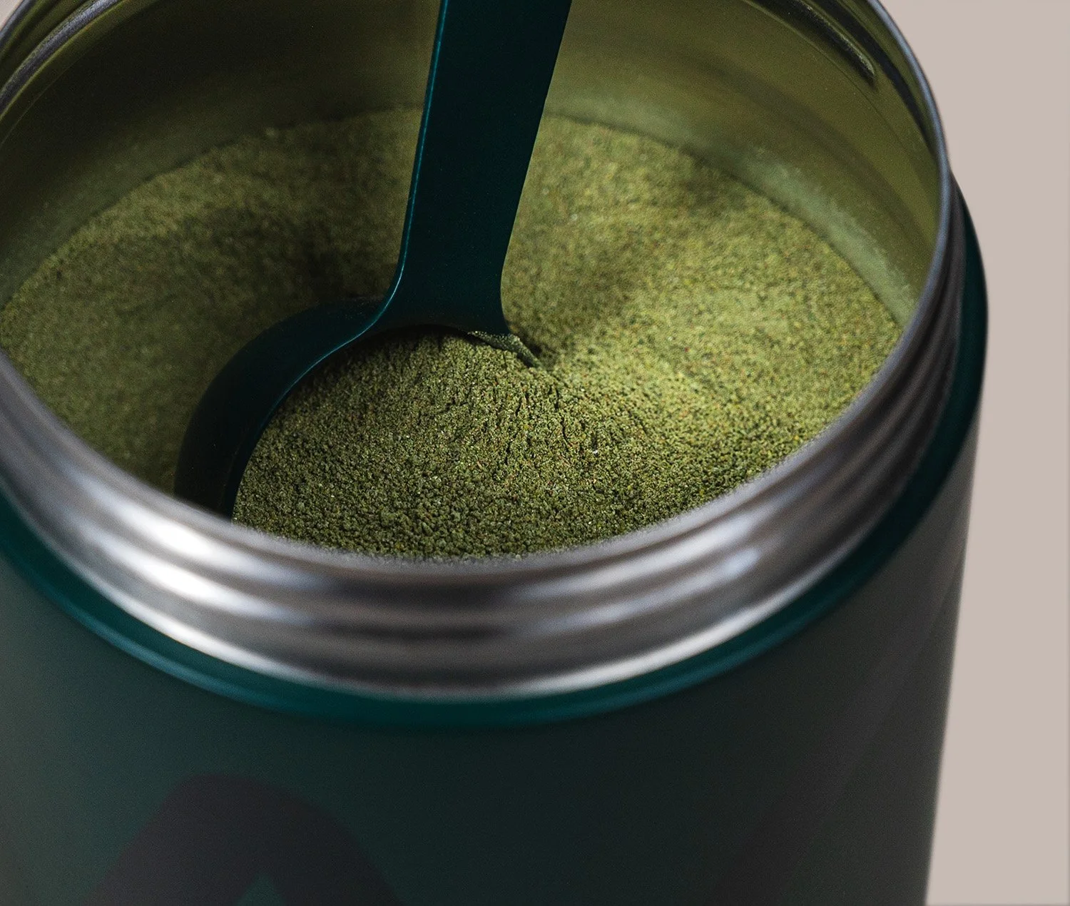 An open container of green powdered supplement with a scoop inside.