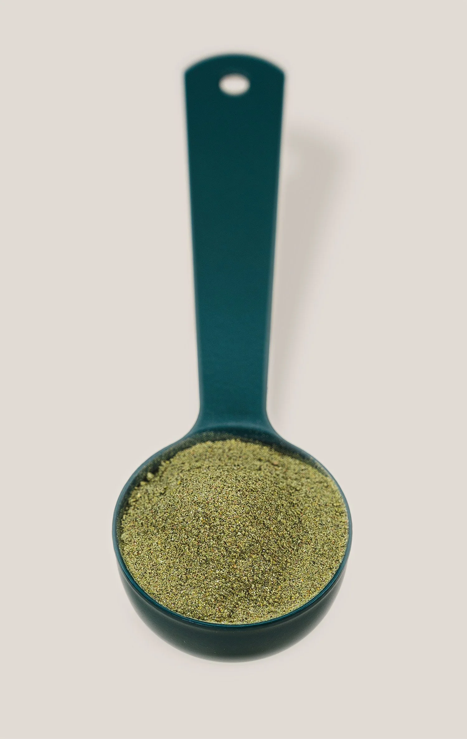 A black measuring spoon filled with a greenish-brown powdered spice.