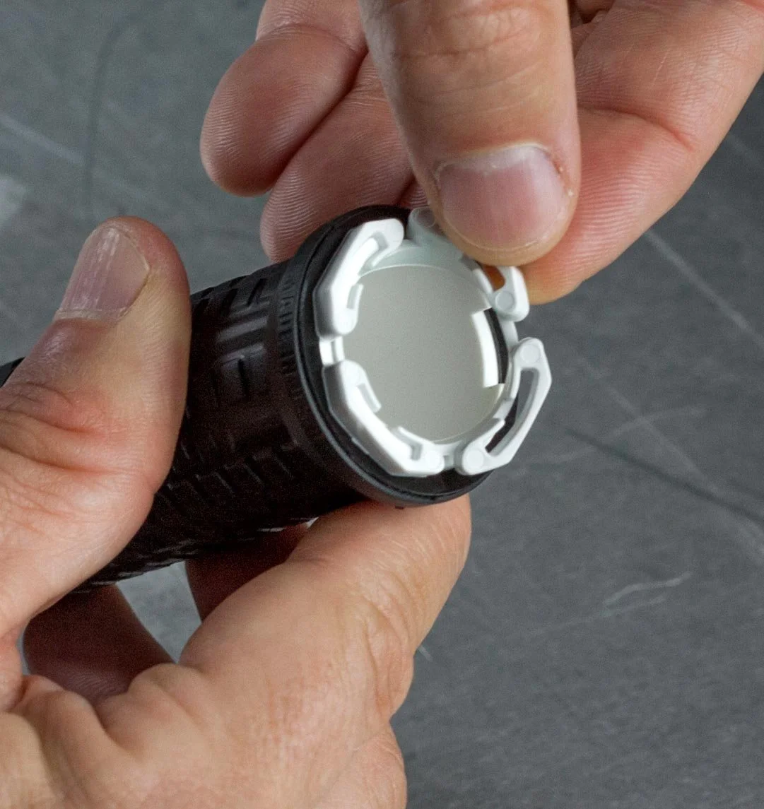 Close-up of hands removing a white battery cover from a black flashlight.
