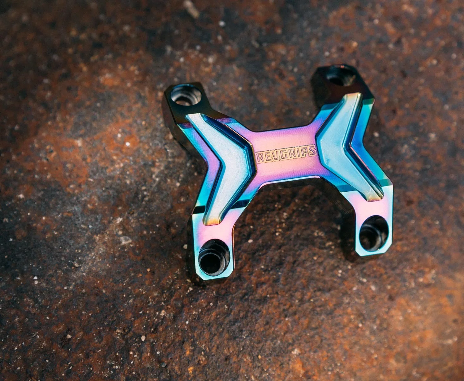 Colorful, iridescent metal bike component with the brand name 'Reverips' engraved, placed on a rusty surface.