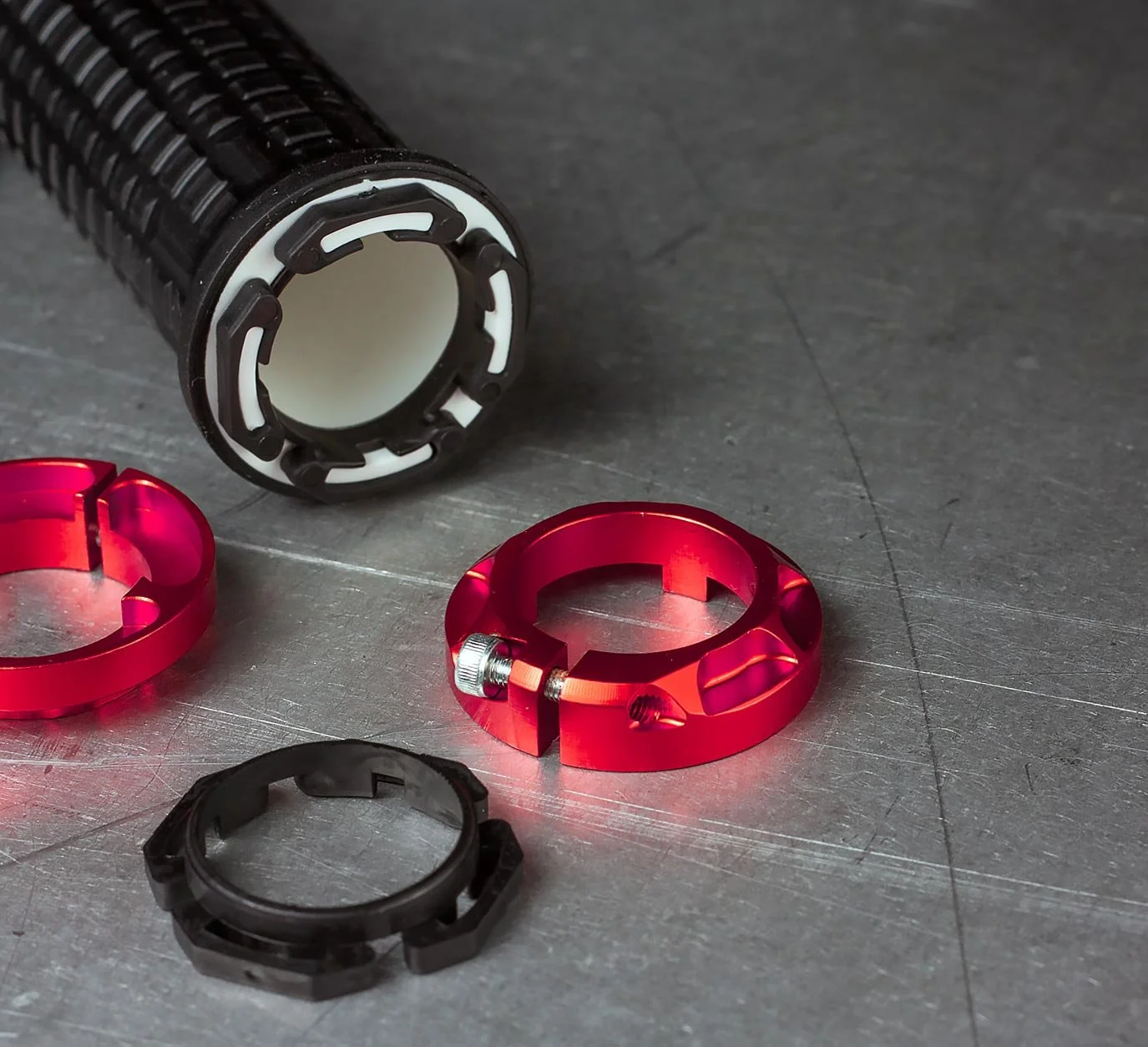 Close-up of motorcycle handlebar grip and red anodized aluminum lock rings on a metallic surface.