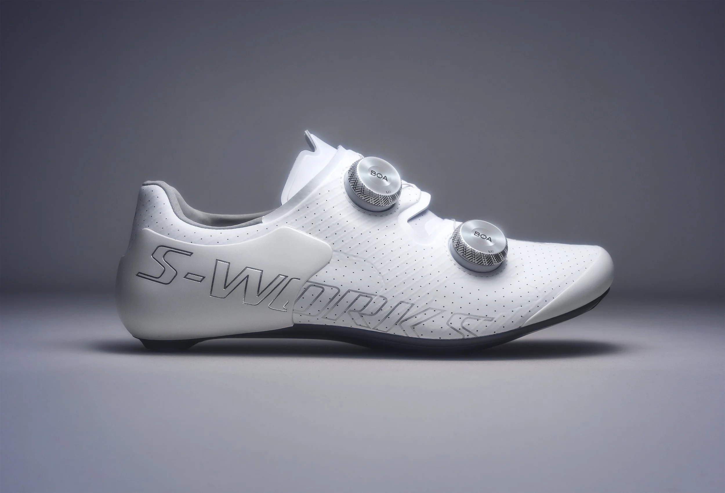 A white racing shoe with the Nike logo and BOA dial closures, set against a plain gray background.