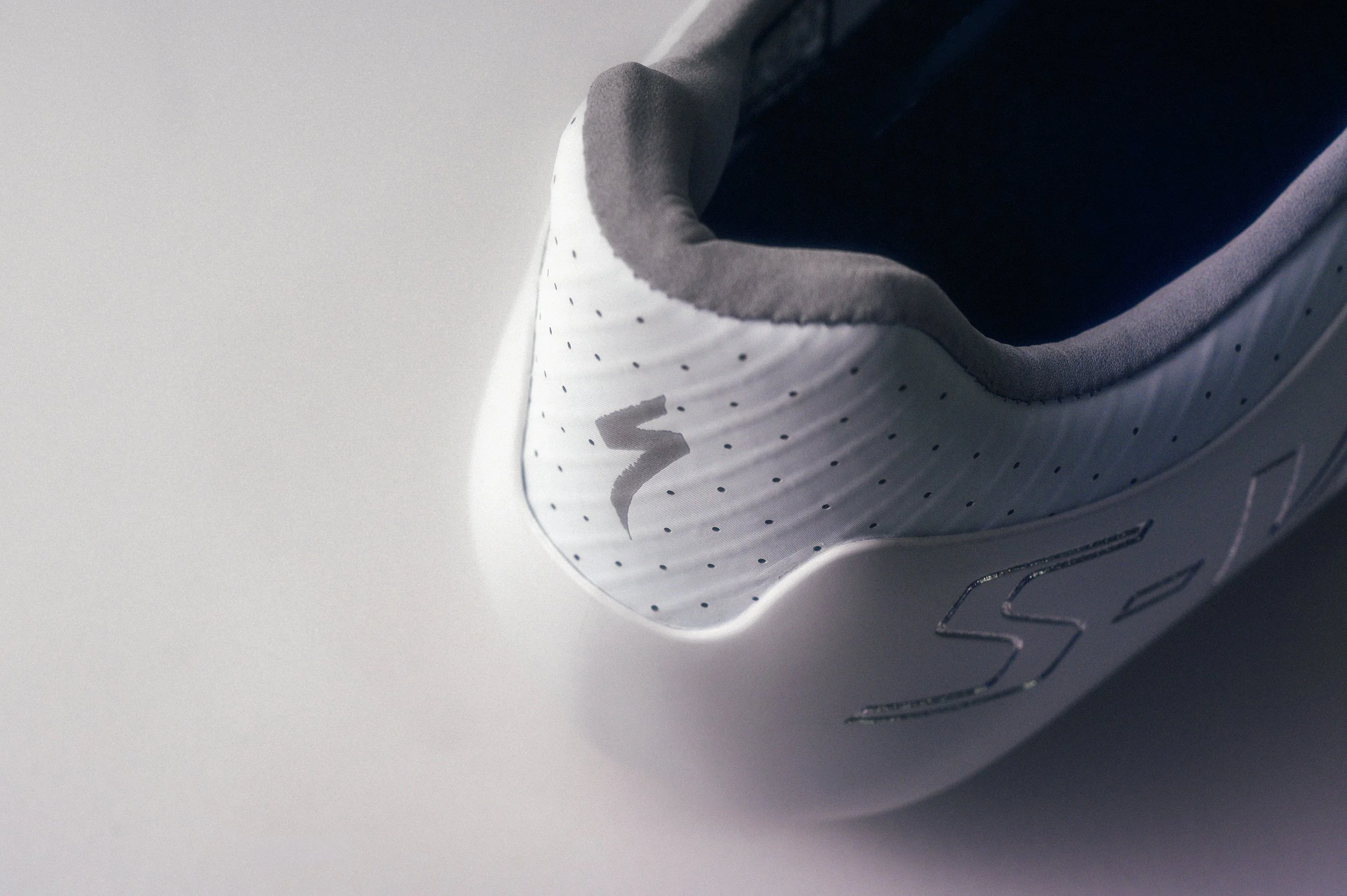 Close-up of a white Nike sneaker with black accents and dotted pattern, viewed from the side on a plain gray background.