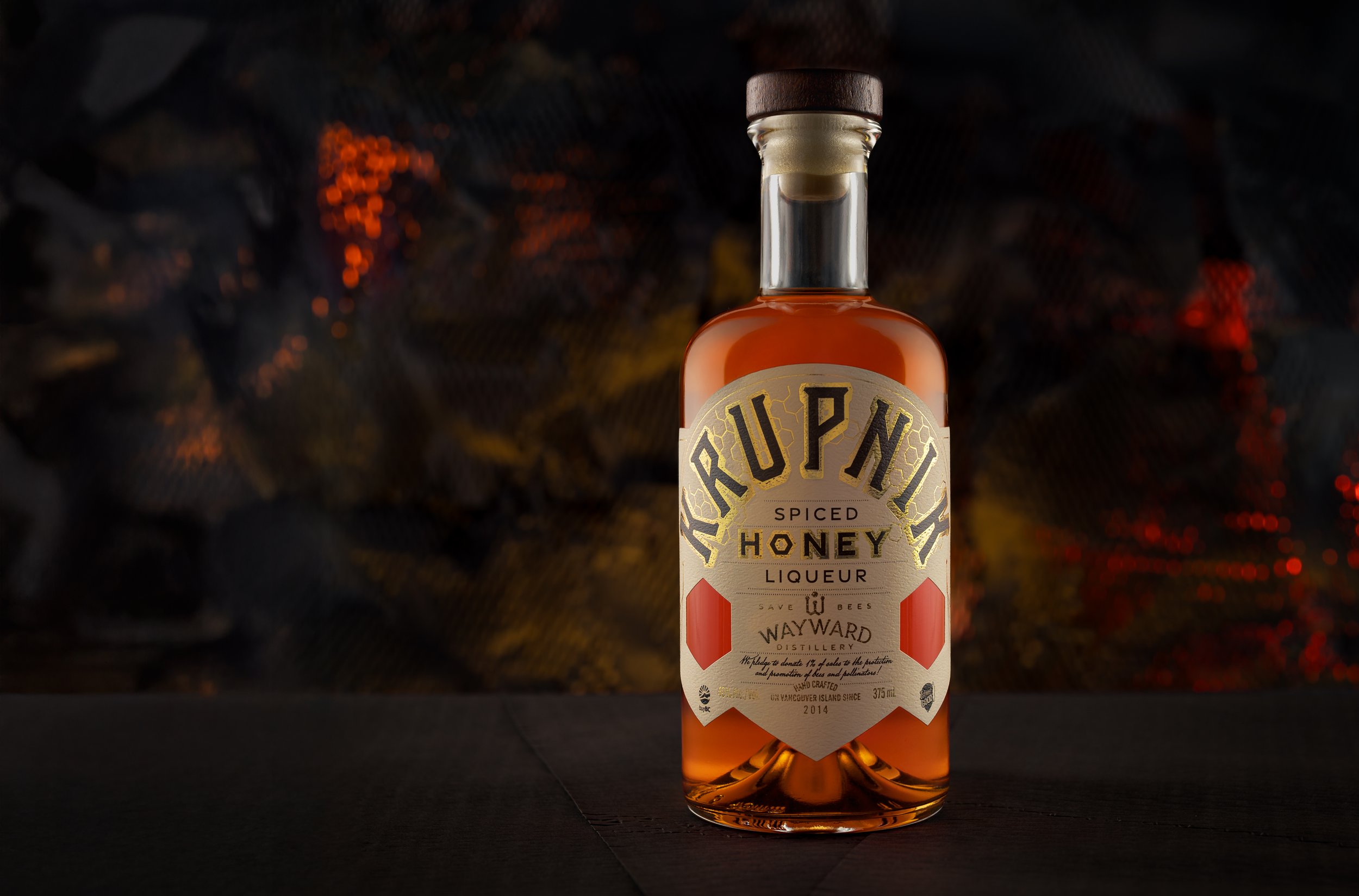 A bottle of spiced honey liqueur labeled 'Run Wild Honey Liqueur' with a dark, blurred background featuring red and yellow lights.