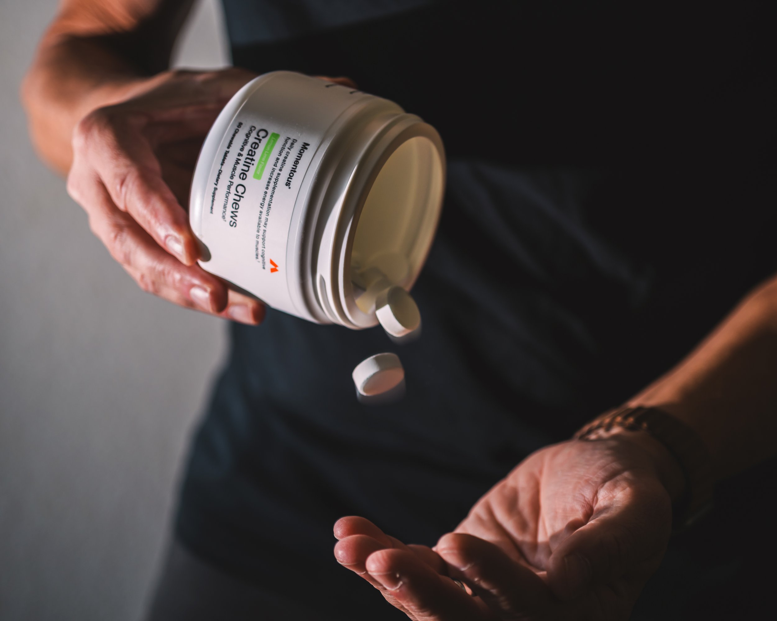 A person with wrinkled hands holding a container of cream, with some of the cream being removed from the container.