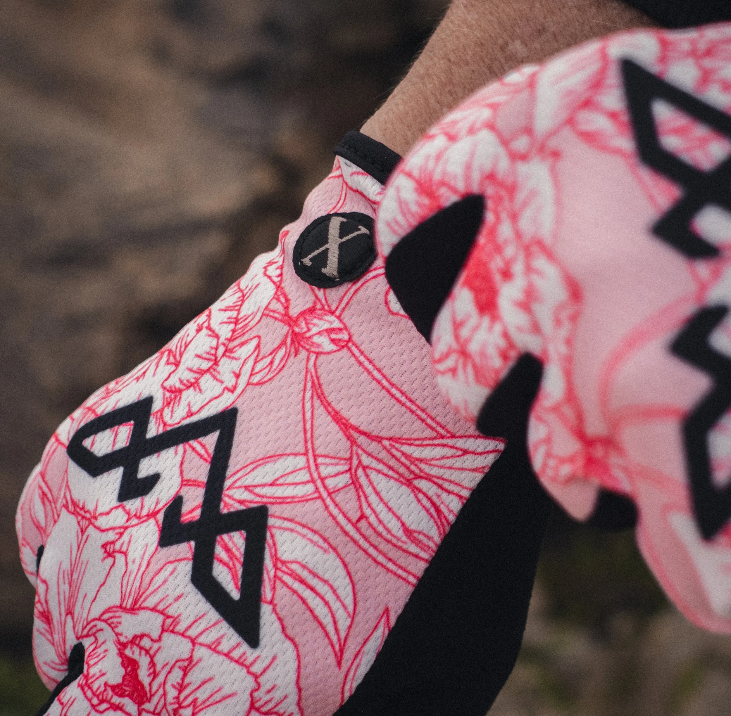 Close-up of a person wearing pink and black athletic shoes with a floral pattern and logo, standing on a dirt path.